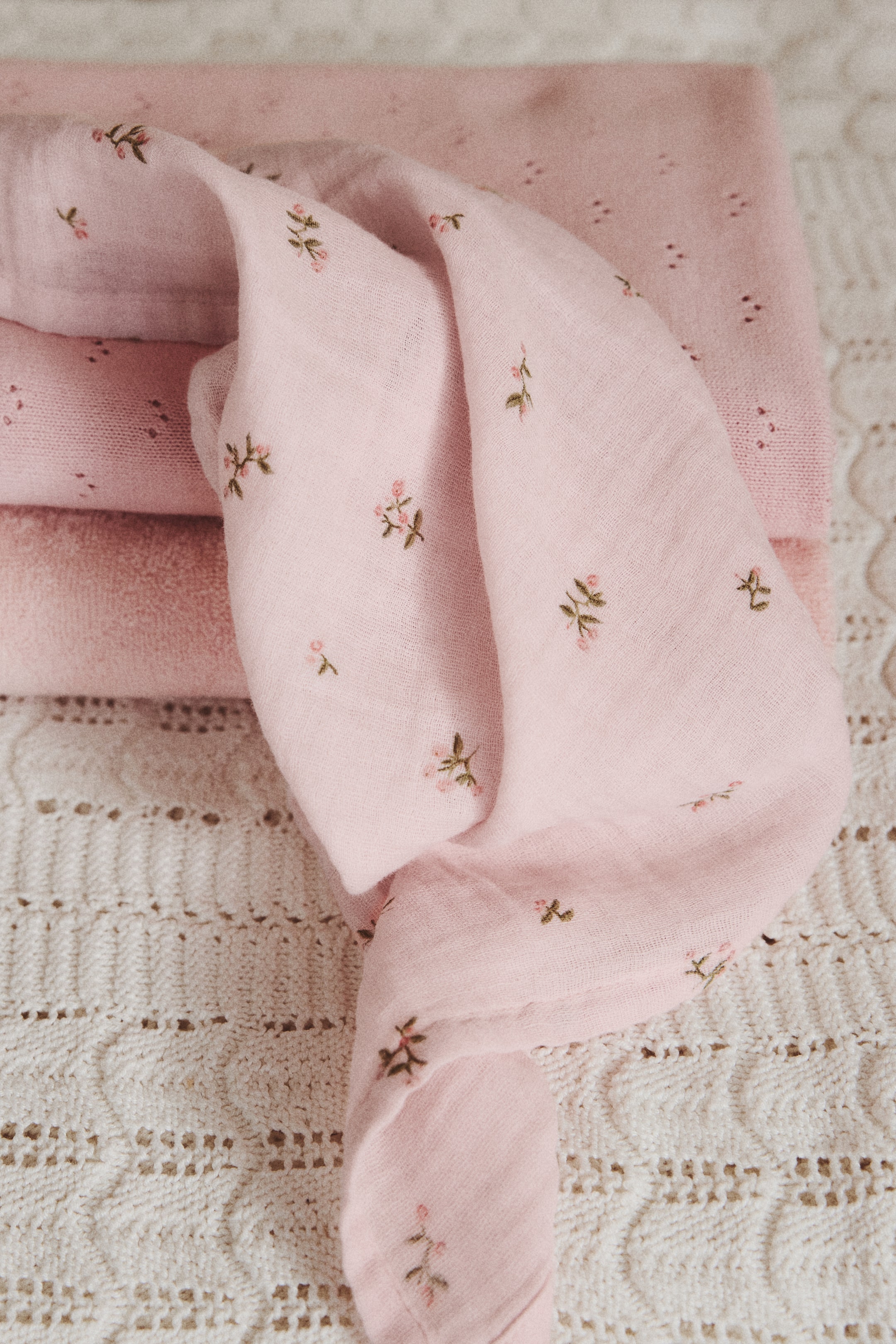 View larger image: A soft pink cotton muslin cloth, adorned with delicate embroidered pink floral patterns, is elegantly draped over a stack of other pink fabrics. The front of this embroidered cloth is prominently displayed, resting on the layered textiles that showcase a variety of textures.