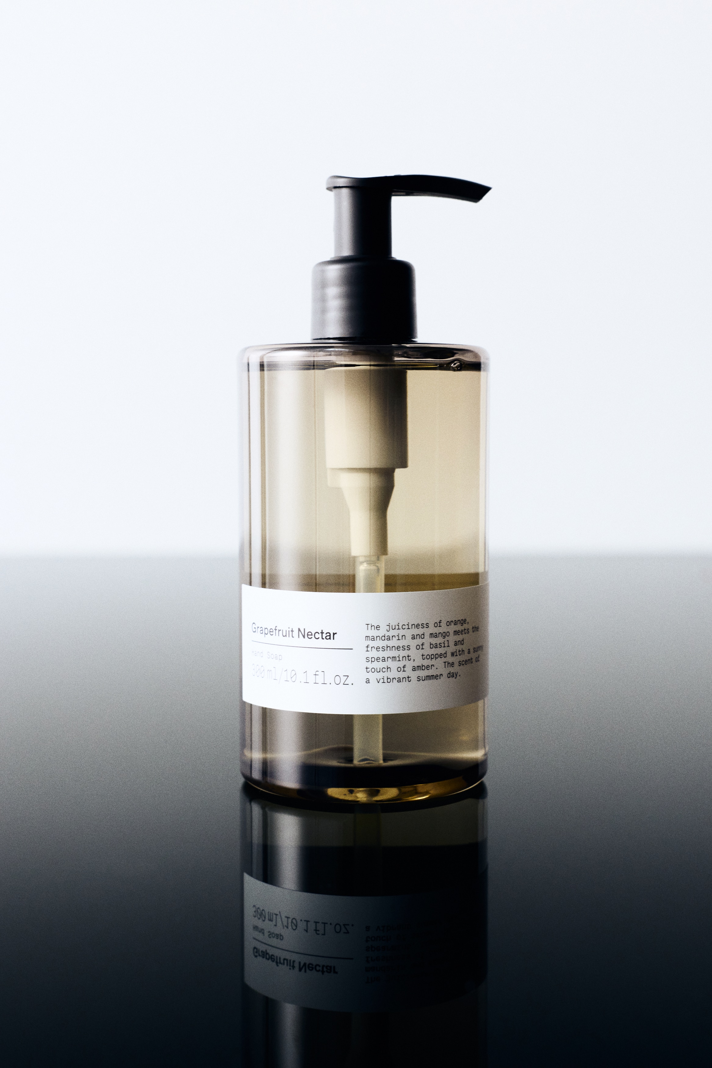 A 300 ml cylindrical bottle of hand soap is standing upright in a front-facing view, showcasing a translucent, amber-tinted plastic container and a black pump dispenser. A white rectangular label is wrapping around the lower half of the bottle, displaying the product name "Grapefruit Nectar" and volume details.