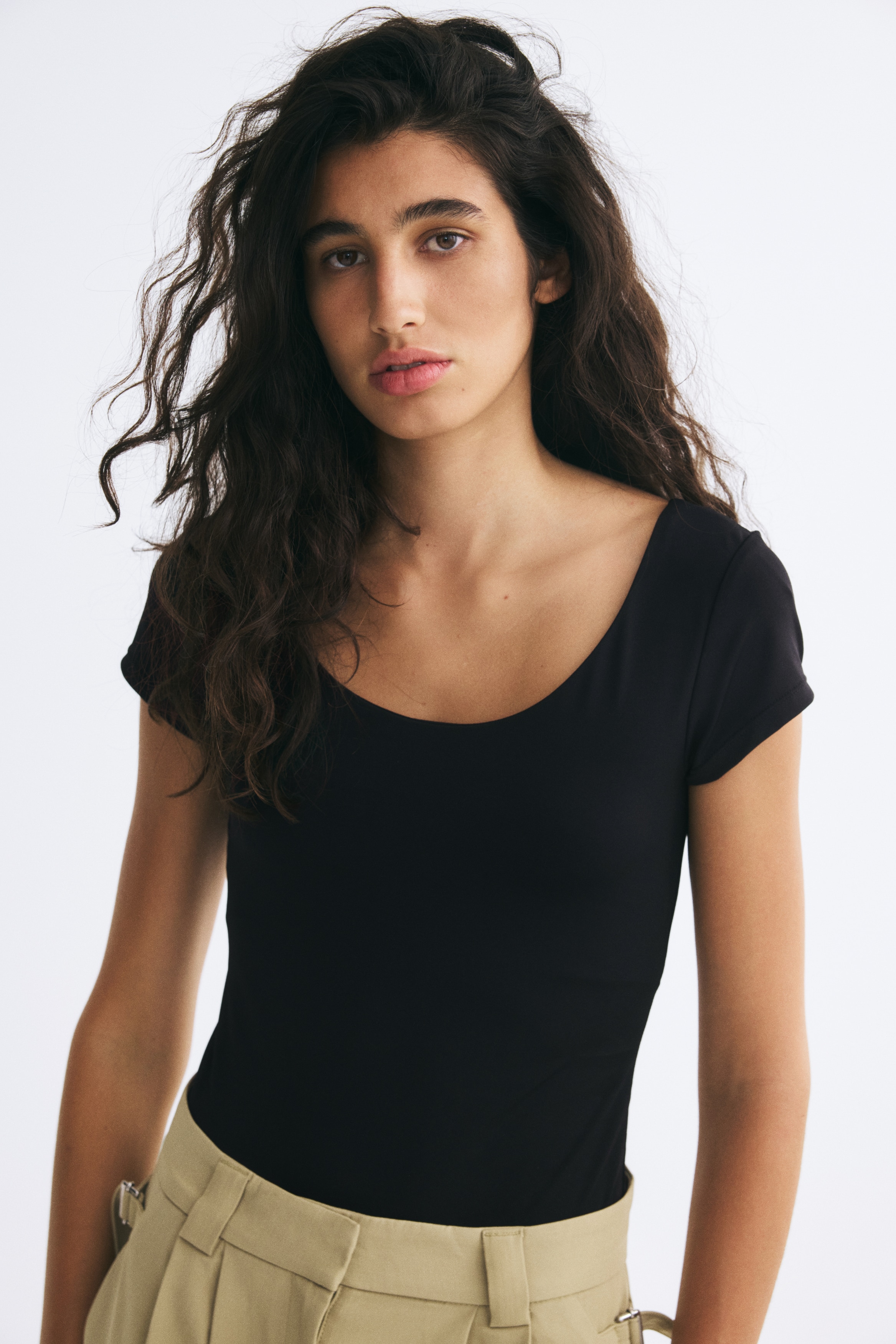 A black bodysuit is facing front, featuring a wide scoop neckline, short cap sleeves, and a fitted bodice. The design is showcasing high-cut leg openings with a thong-style bottom.