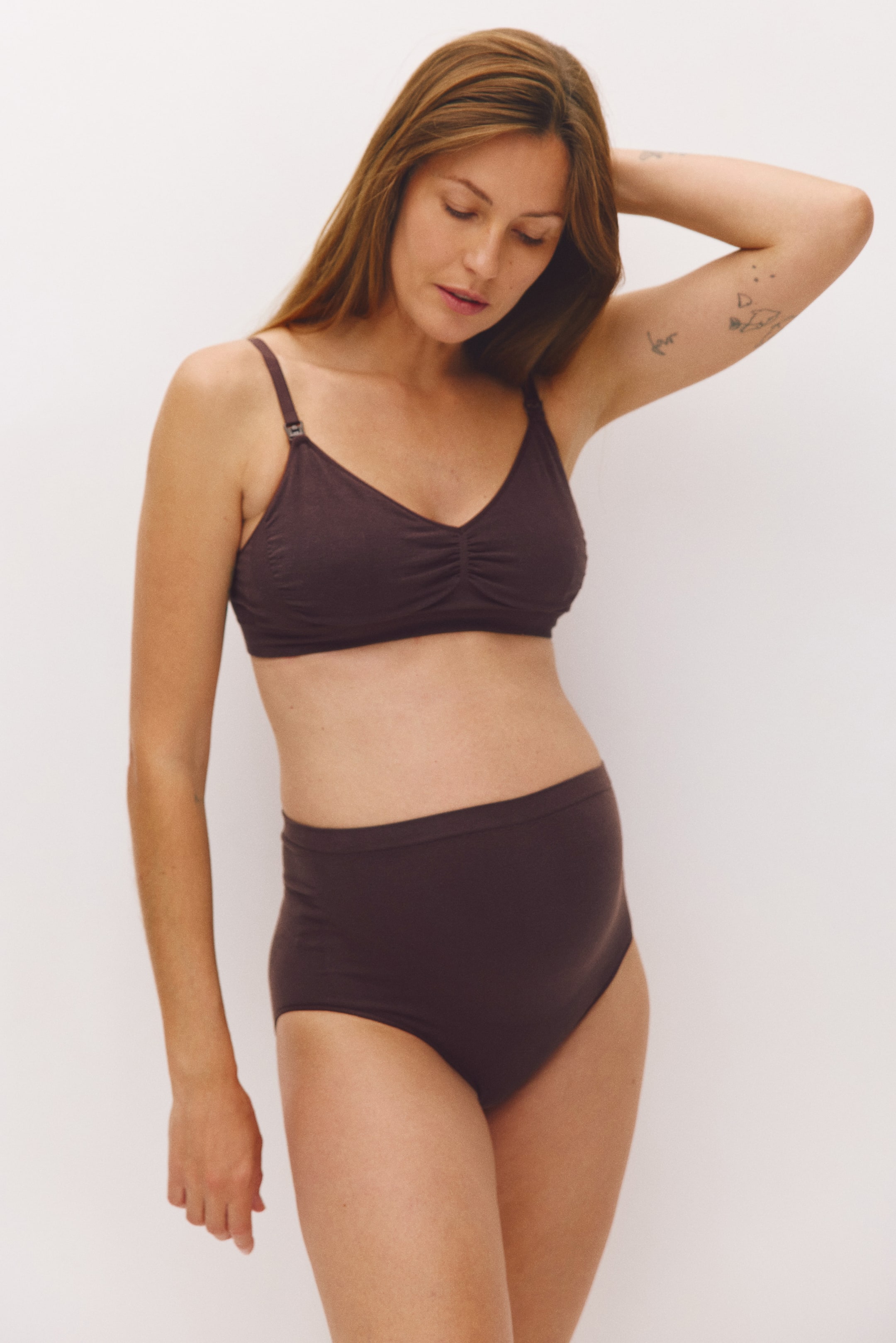 View larger image: A dark brown, wireless nursing bra featuring a gathered centre bust and adjustable shoulder straps is being worn by the model. The bra is styled with matching high-waisted briefs.