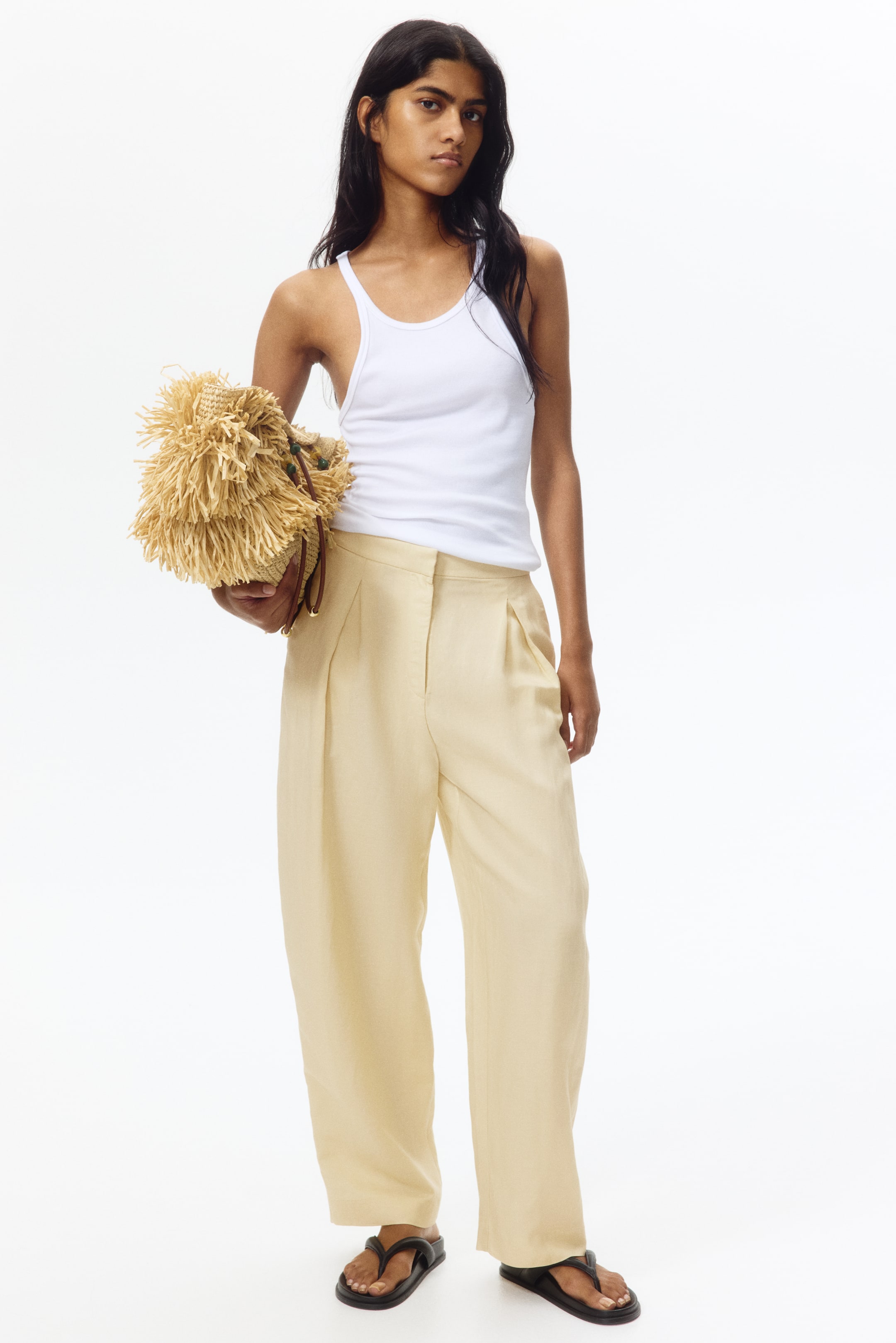 View larger image: Light yellow high-waisted pants featuring front pleats and wide, flowing legs, facing forward. They extend to the ankles, showcasing a relaxed fit.