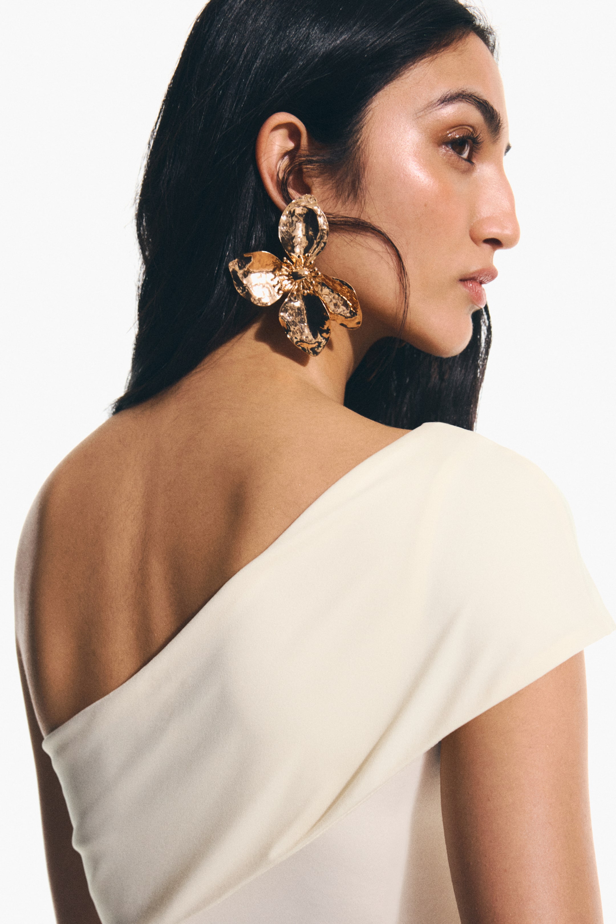 View larger image: "Flower-shaped earrings crafted from metal with a subtly hammered finish are showcased on the model's ear."