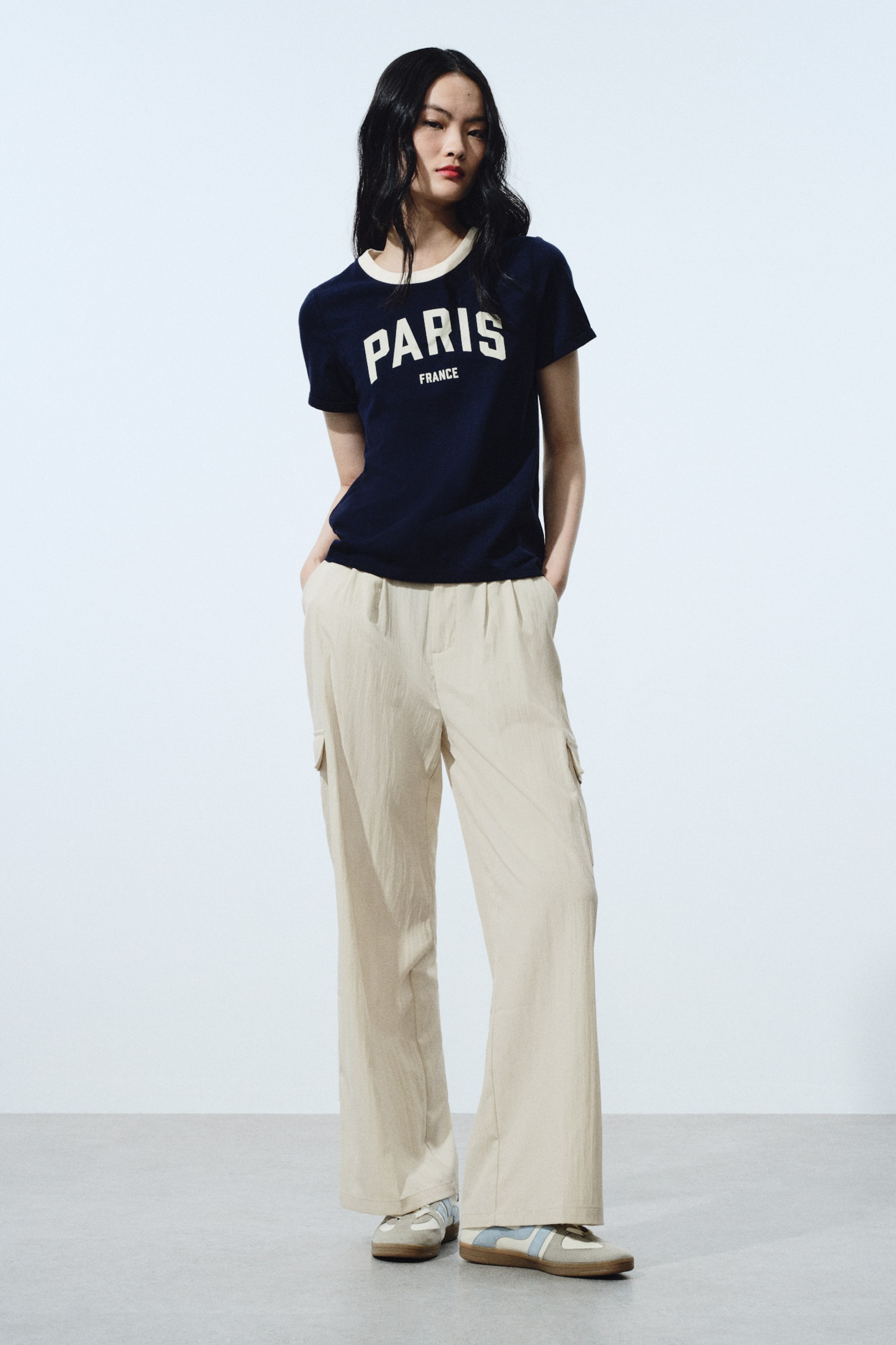 View larger image: A navy‑blue T‑shirt featuring a white "PARIS FRANCE" graphic on the front and a contrasting off‑white round neckline. It is paired with light‑beige wide‑leg cargo trousers featuring an elasticated drawstring waist and side cargo pockets.