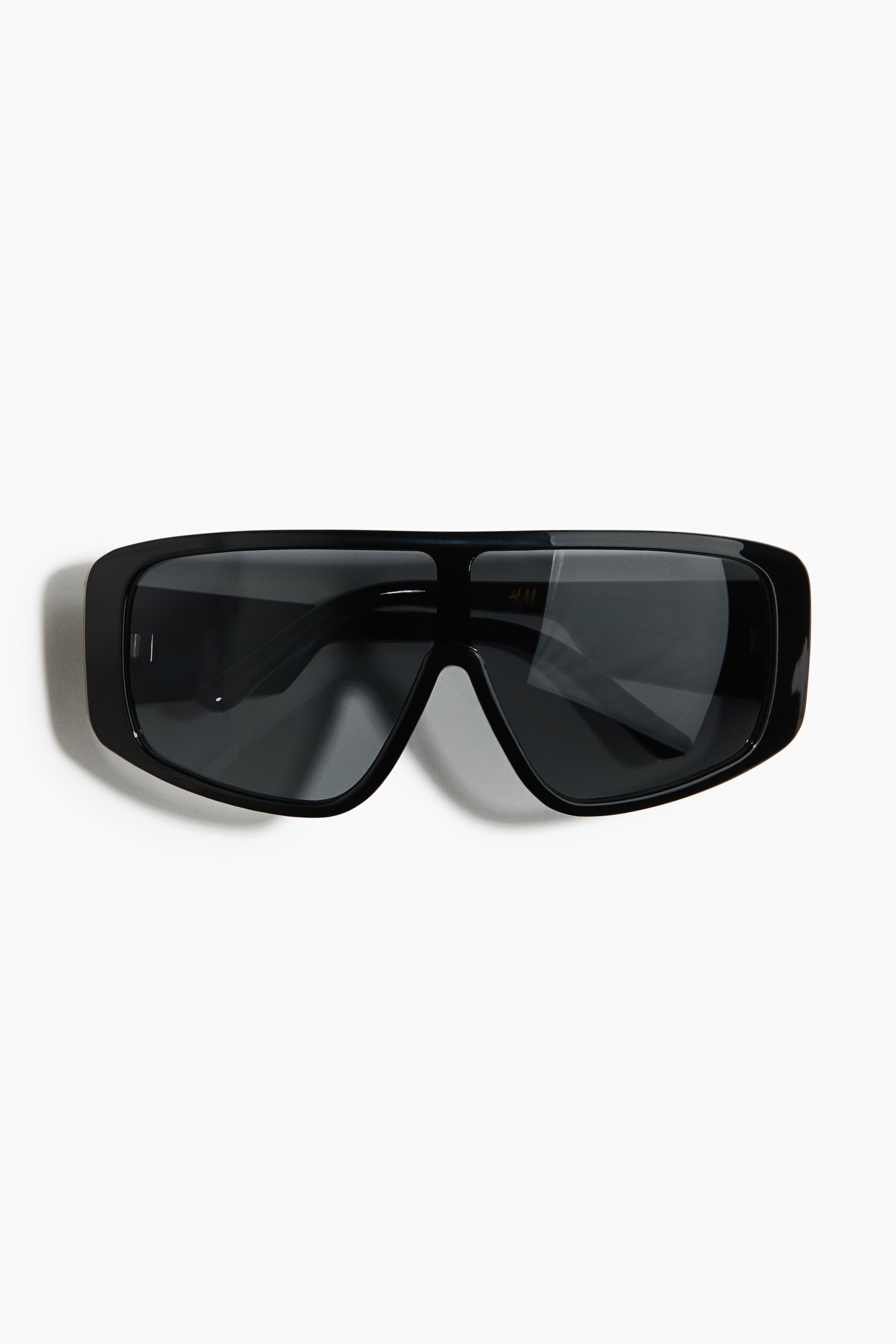 View larger image: Visor sunglasses are lying flat and facing forward, featuring a black plastic frame with wide sidepieces. They are fitted with tinted, UV-protective plastic lenses.