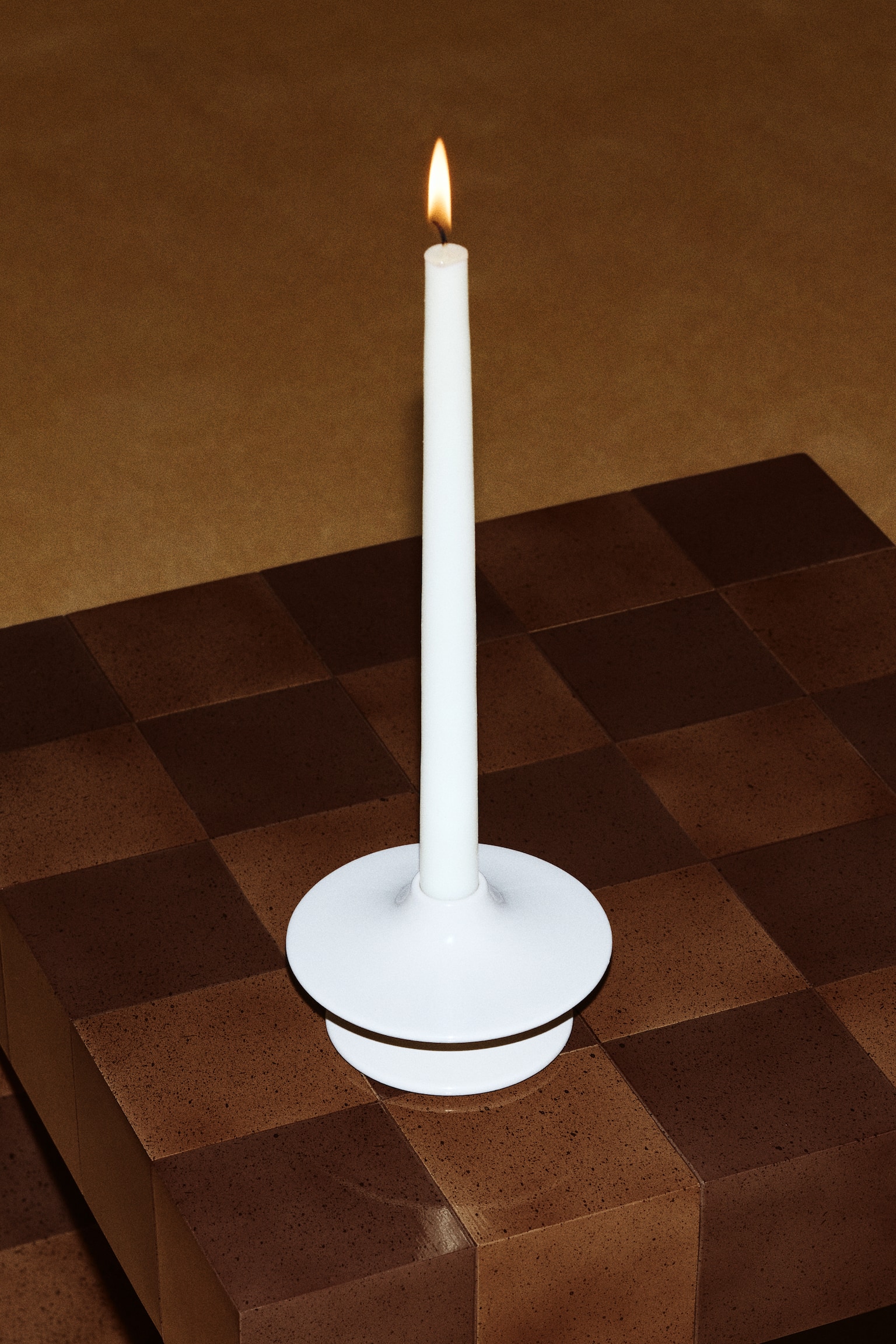 A light beige ceramic candlestick is holding an off-white tapered candle, featuring a circular base and a wide, flat top with a subtly curved, upward-sloping edge. - 1