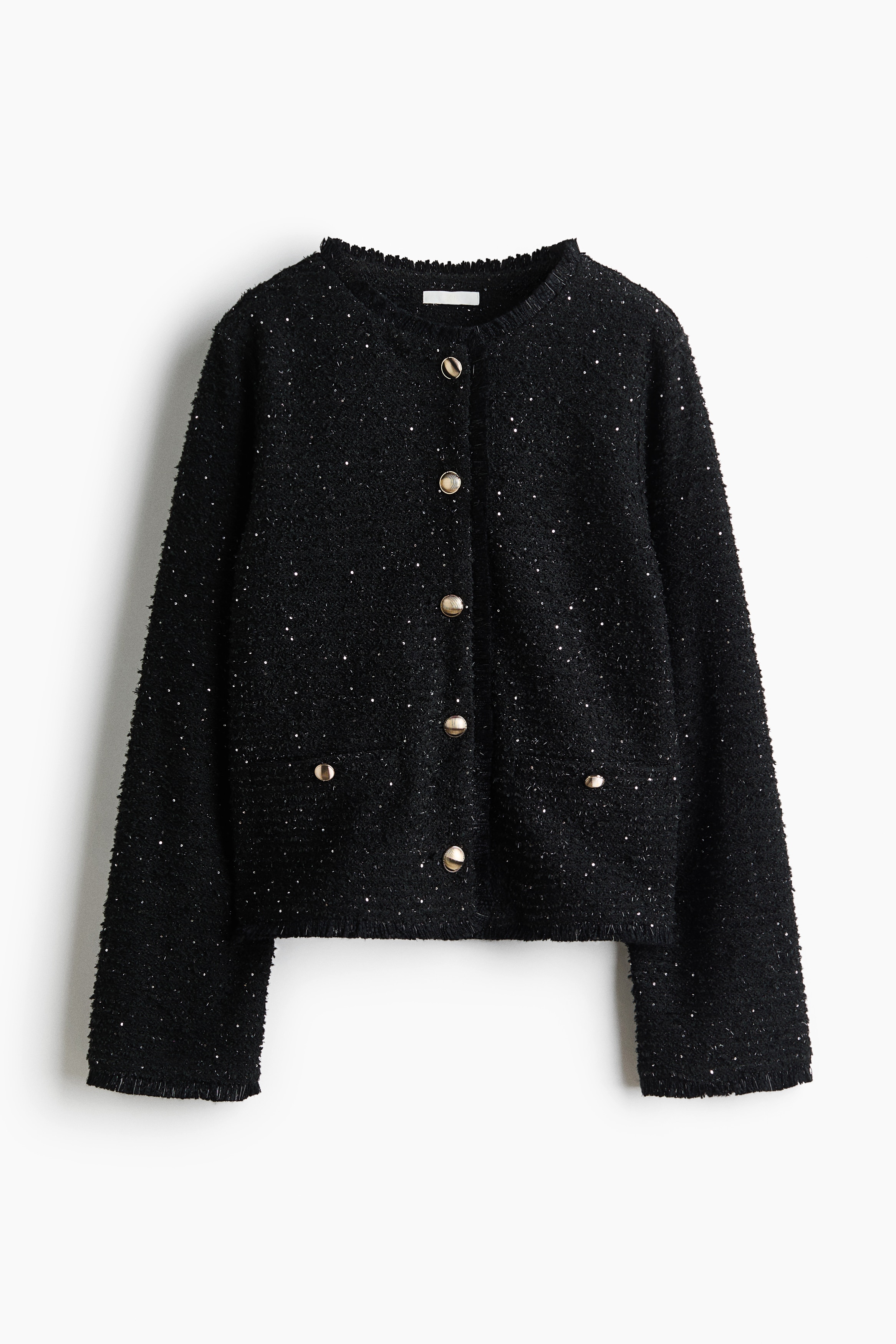 A black textured tweed jacket with subtle sequin embellishments and gold-tone buttons is worn by the model. The jacket is layered over a black top and paired with wide-leg blue jeans and black pointed-toe heels.