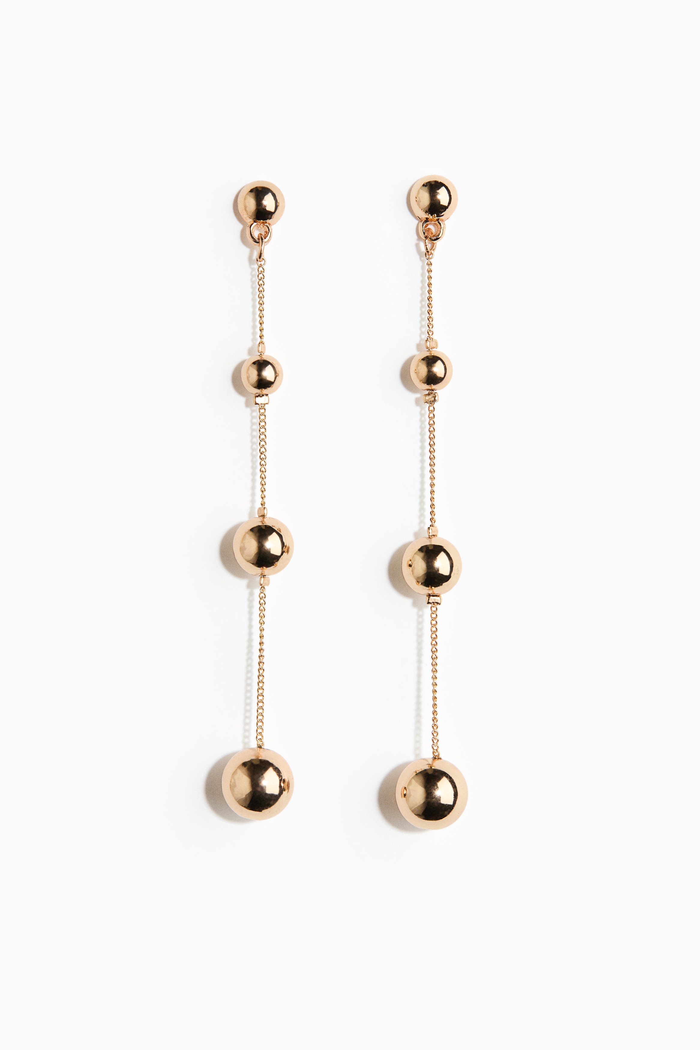 A long metal chain earring featuring evenly spaced gold-toned plastic beads that increase in size towards the bottom is being worn on the ear of the model. The earring is hanging down alongside a black turtleneck top.