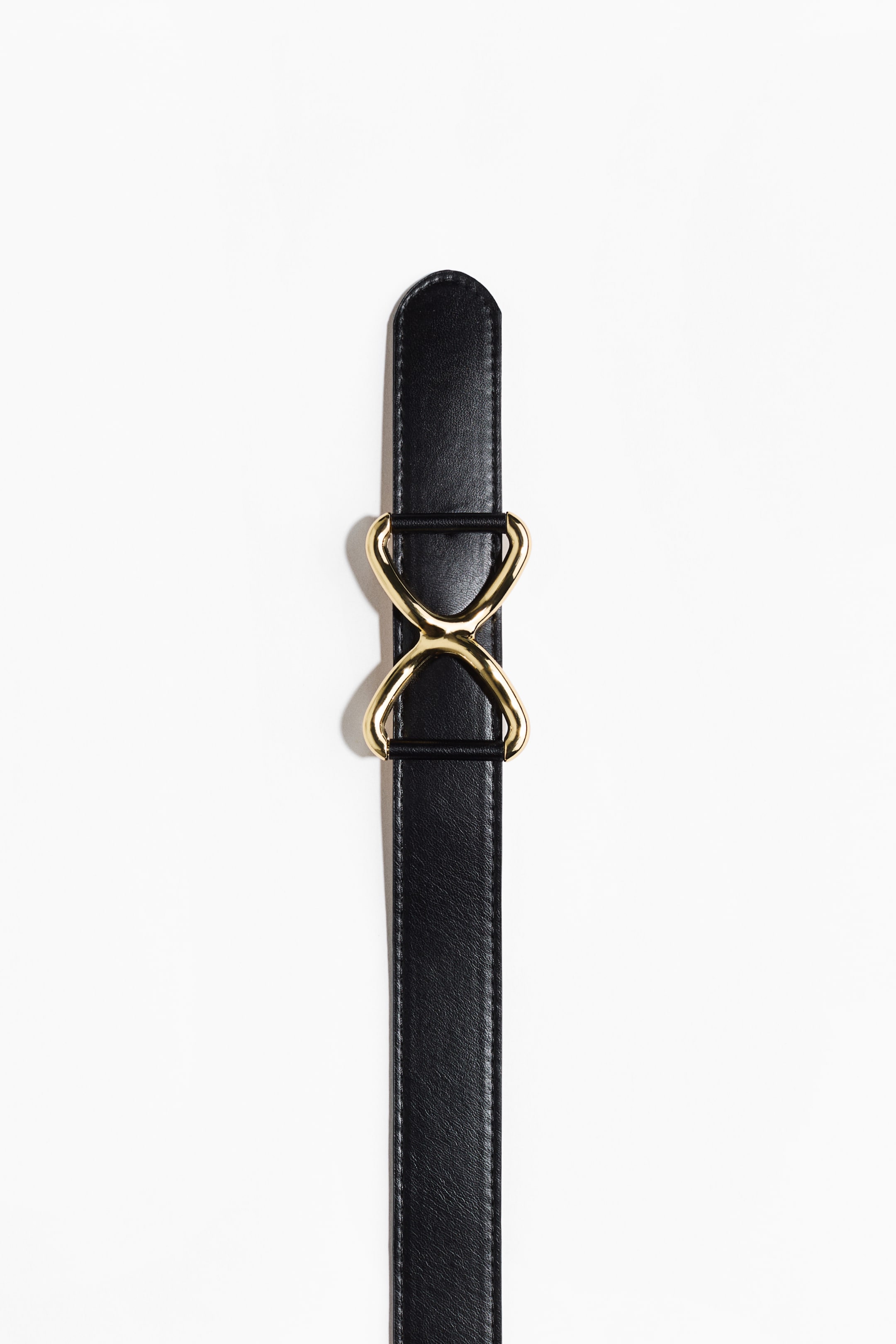 View larger image: A narrow black belt is featuring a gold-toned, figure-eight metal buckle.