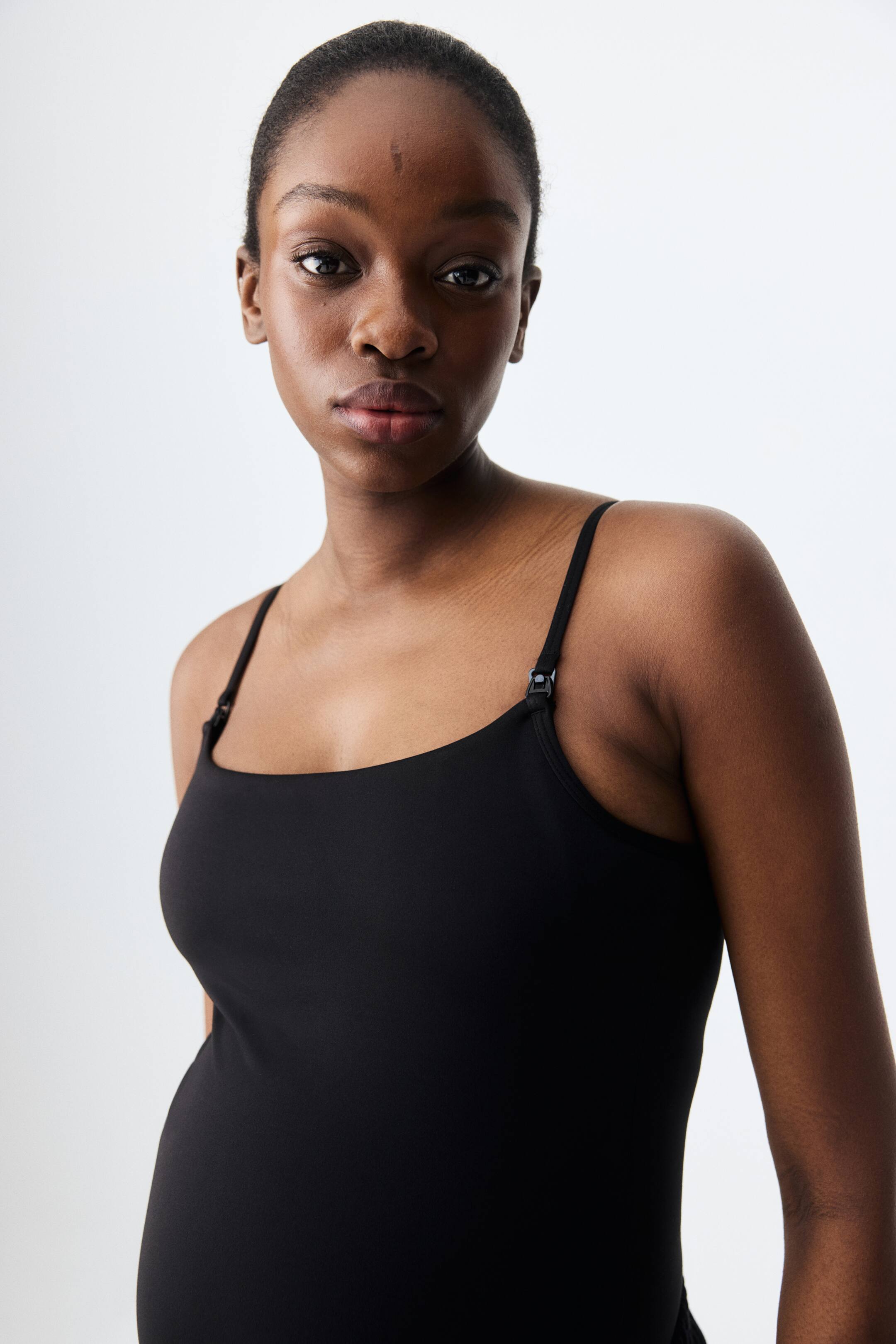 Ampliar la imagen: Se está usando una blusa negra estilo camisole, que presenta tirantes delgados ajustables con broches negros para lactancia visibles cerca de los hombros.