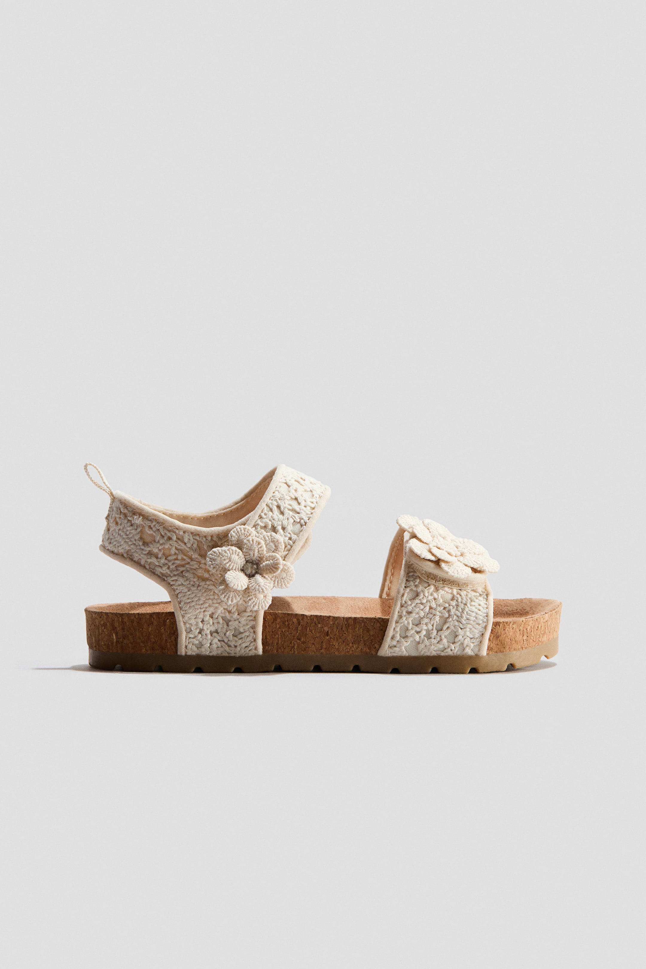 View larger image: These strap sandals feature cream-colored crocheted straps adorned with floral appliqués. An adjustable fastening appears on the ankle strap, and the sandals showcase molded insoles with fluted soles.