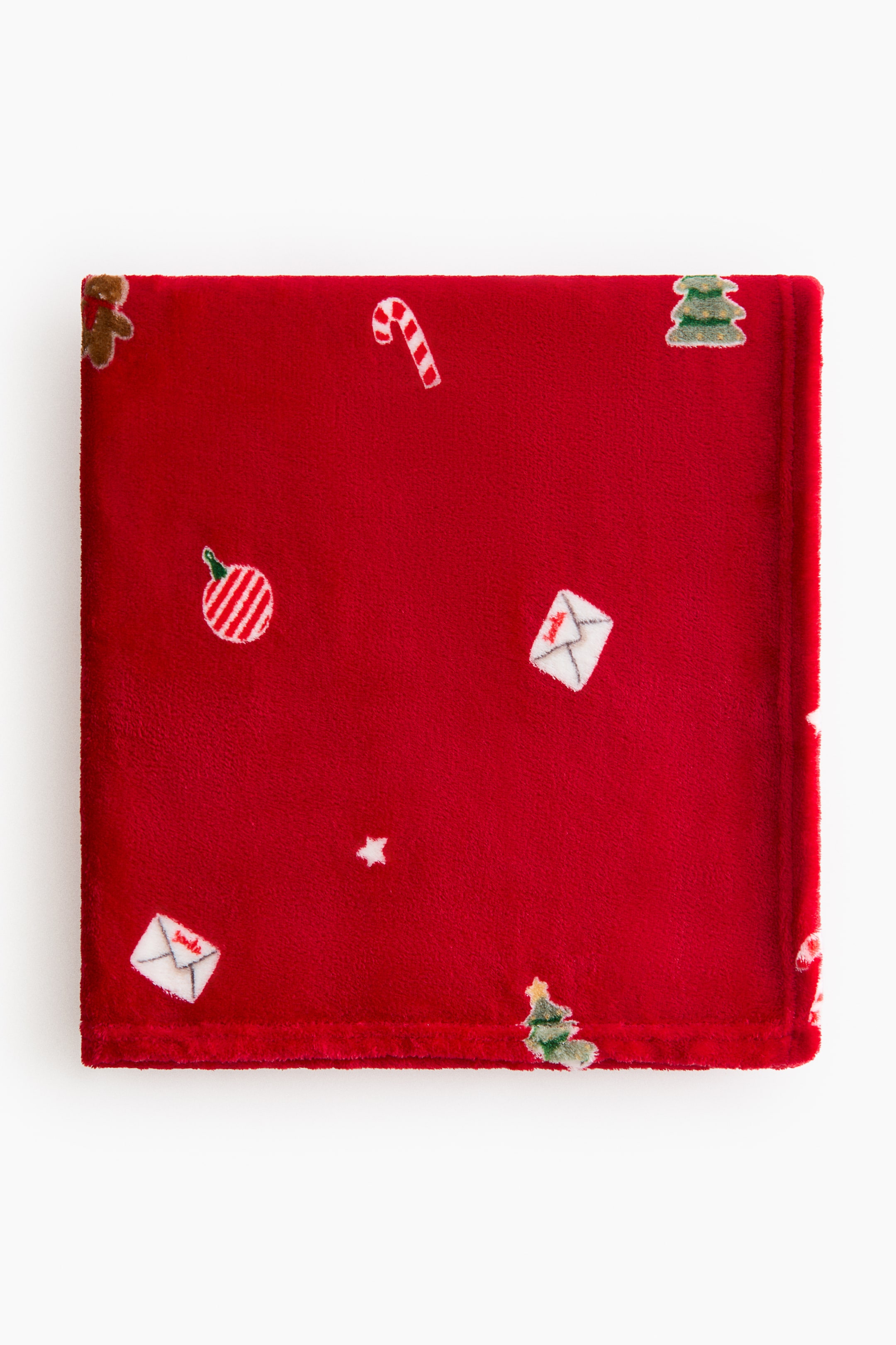 Ampliar la imagen: Una manta de felpa roja está doblada y extendida, mostrando un patrón de motivos navideños dispersos, que incluyen hombres de jengibre, bastones de caramelo, adornos, cartas a Santa, estrellas y árboles de Navidad.