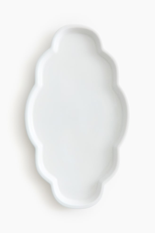 A white dish showcases an elongated, undulating shape with a scalloped edge. Its glossy surface features a subtle raised rim. - 1