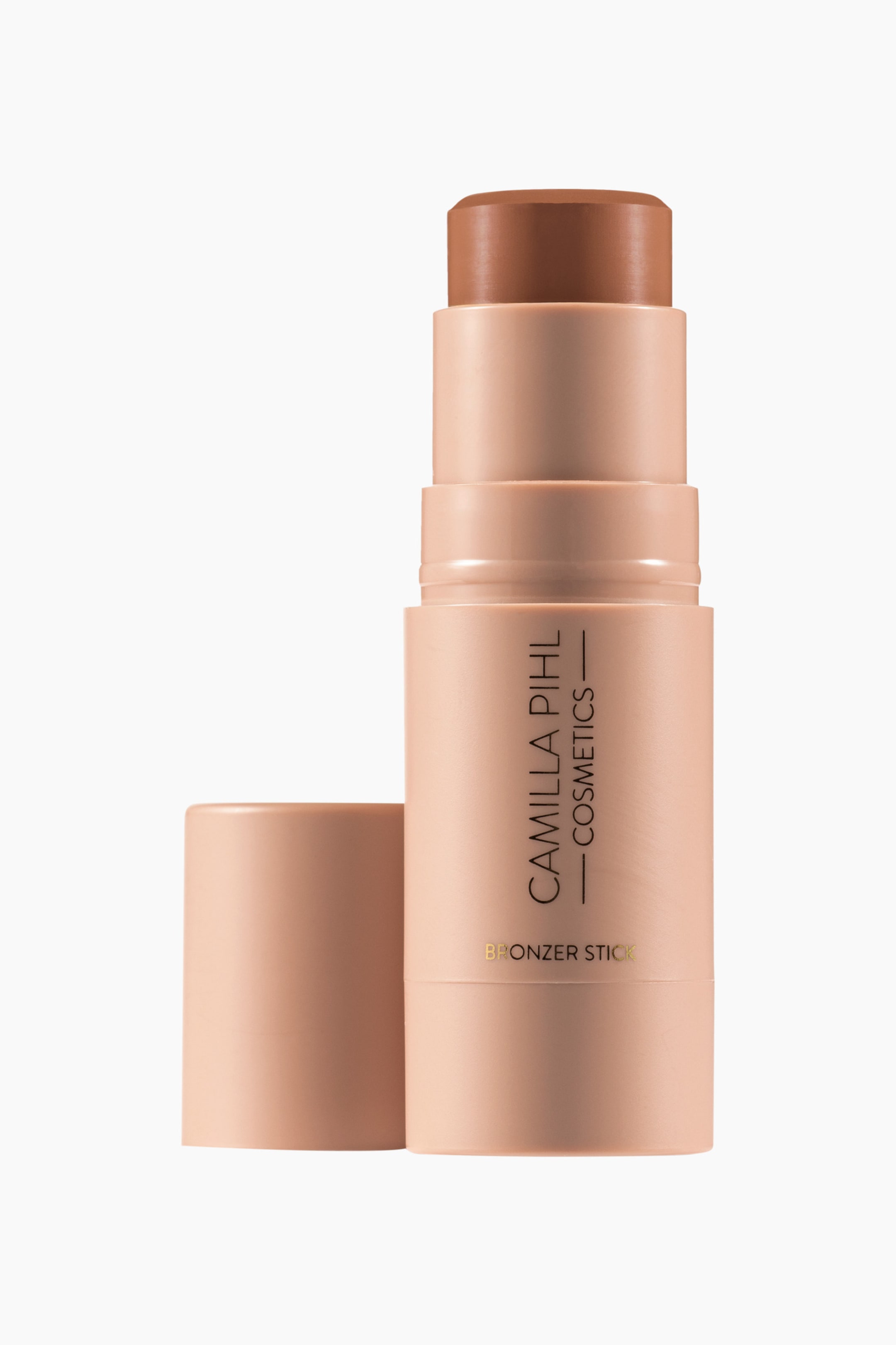 Visa större bild: En bronzer-sticka står upprätt och är något vinklad åt höger, med dess ljusa persikobeige lock borttaget och vilande bredvid basen. En medelbrun, cylindrisk bronzerprodukt med en rundad topp sträcker sig från stickans ljusa persikobeige hölje, som visar "CAMILLA PIHL COSMETICS" vertikalt och "BRONZER STICK" horisontellt.