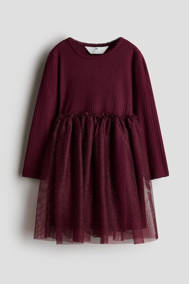 A dark burgundy dress is shown facing front, featuring a long-sleeved, ribbed jersey bodice with a round neckline and picot trims at the collar and cuffs. The dress is designed with a small frill trim at the waist and a flared, lined tulle skirt that is sparkling with fine glitter. - 1