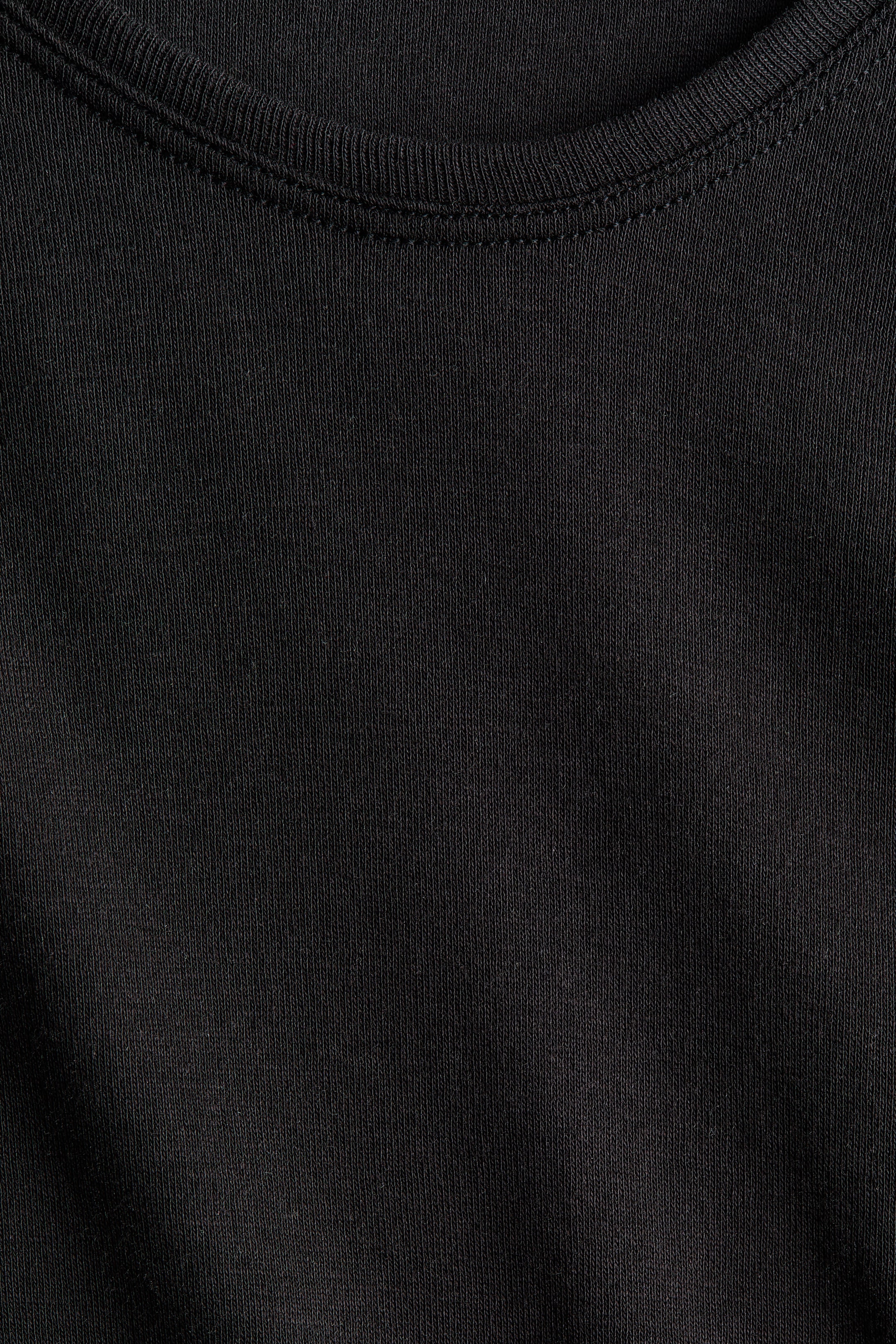 Ver imagem maior: Um top de malha preto apresenta uma gola crew com uma banda canelada. A banda encontra-se costurada de forma segura ao tecido principal, que apresenta uma subtil textura de malha vertical.