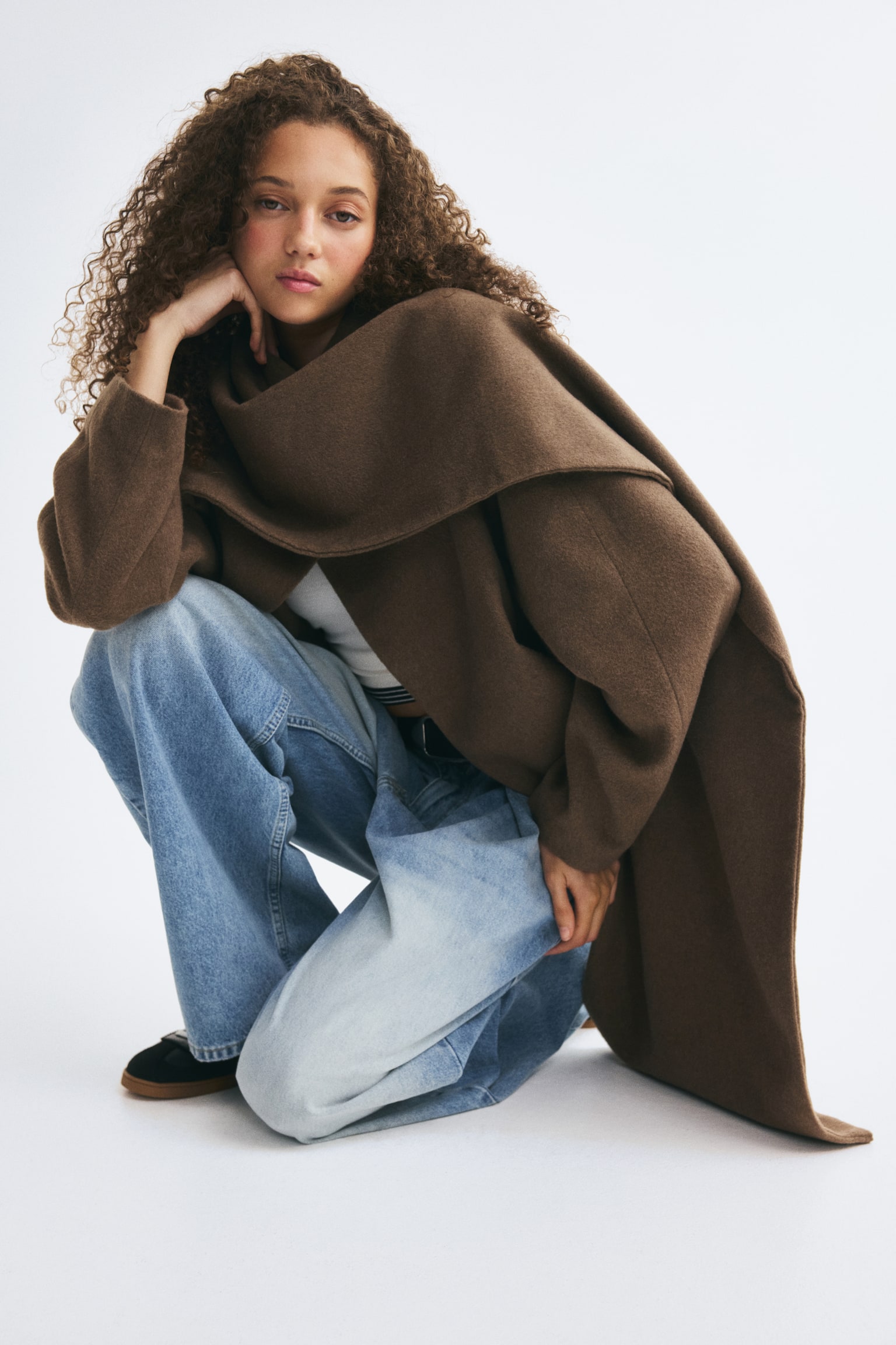 A short, brown wool-blend jacket is hanging front-facing, featuring an integrated draped scarf collar that wraps around the neck. The jacket showcases a button-free open-front design, long sleeves, and a structured, clean-cut hem. - 1