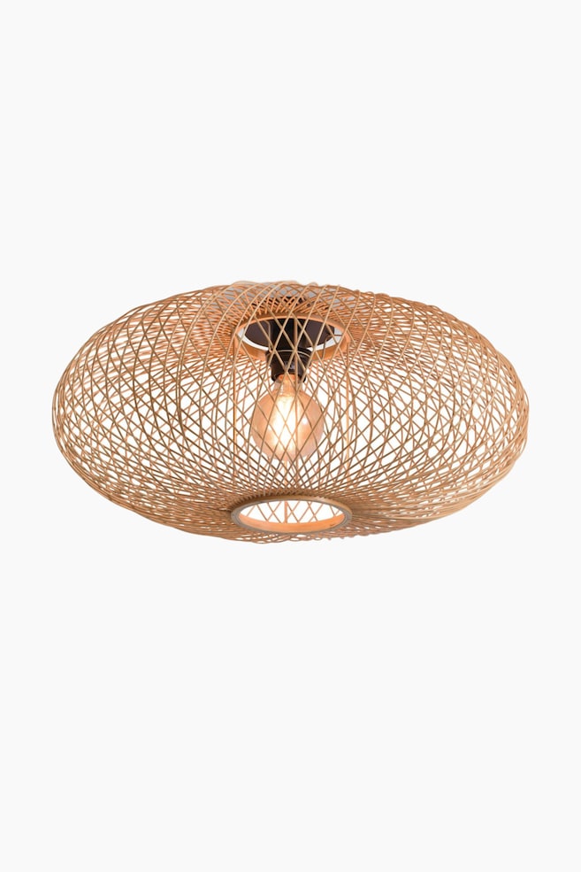 Eine Deckenleuchte zur bündigen Montage mit einem geflochtenen Rattan-Schirm in abgeflachter, ovaler Form und offenem Gittermuster. Eine einzelne, eingeschaltete Glühbirne leuchtet aus der Mitte und ist an einer dunklen Halterung befestigt, die durch die runden Öffnungen oben und unten sichtbar ist. - 1