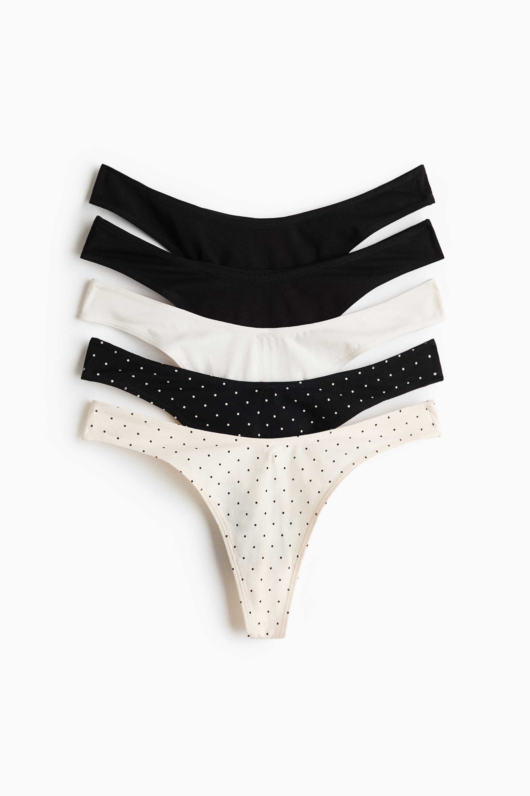 Agrandir l'image: Cinq strings sont disposés à plat et empilés, avec leurs ceintures orientées vers le haut. La pile comprend deux noirs unis, un blanc uni, un noir à pois blancs et un crème à pois noirs.