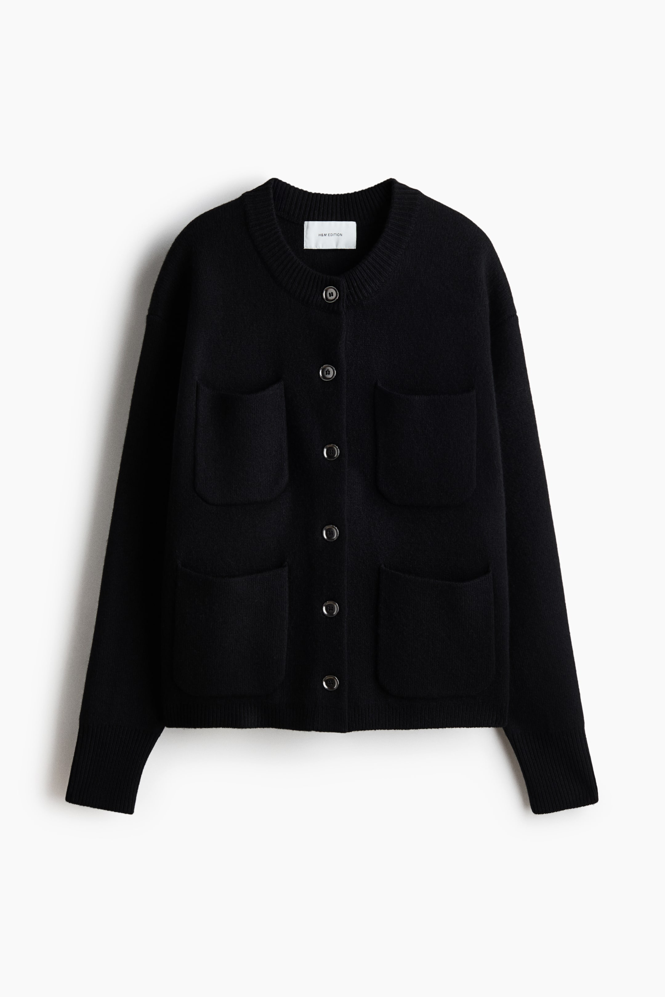 View larger image: A black cardigan is shown from the front, featuring a round, ribbed neckline and a row of dark, round buttons. It is designed with dropped shoulders, long sleeves with ribbed cuffs, a ribbed hem, and four prominent patch pockets on the front.