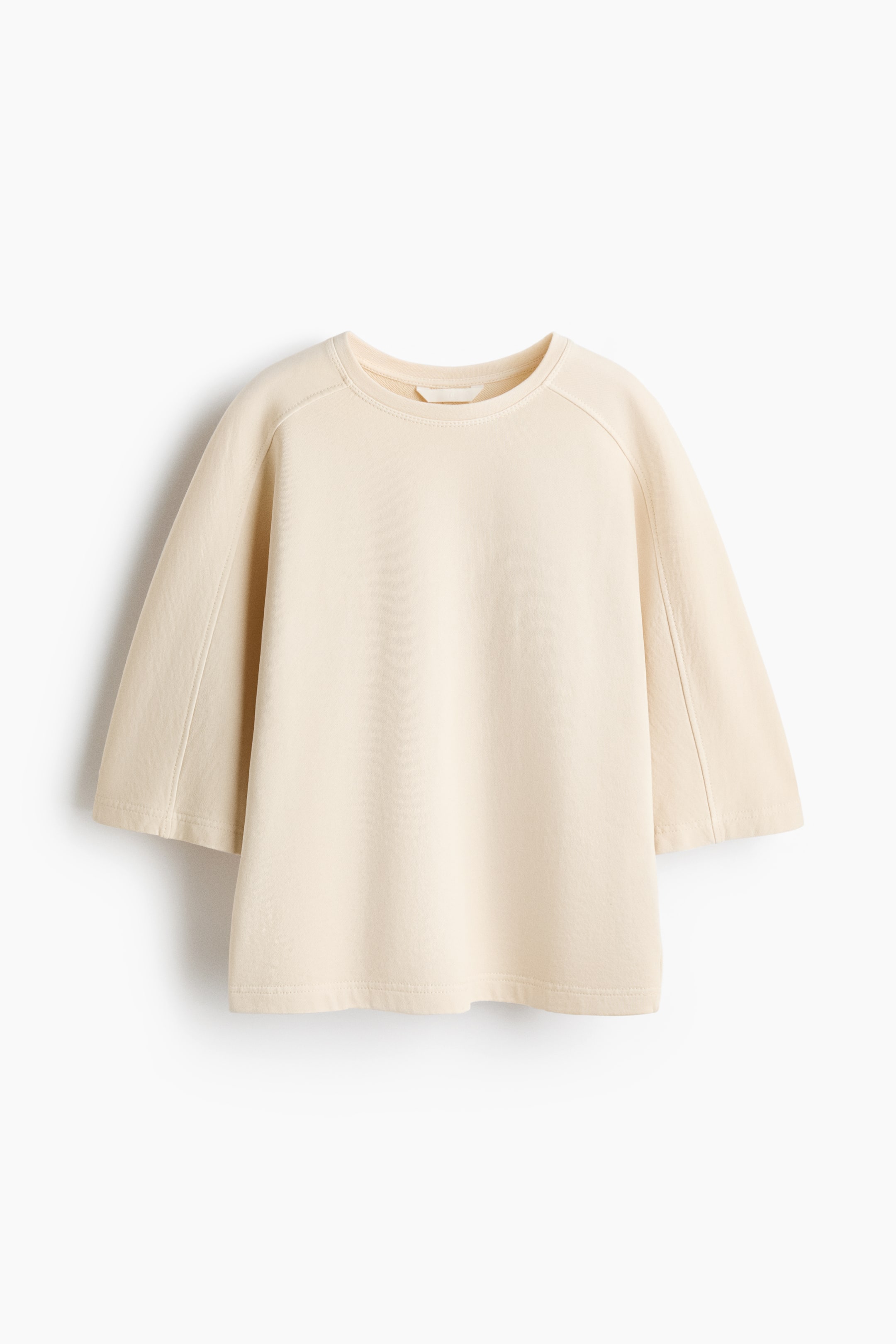 Ver imagen más grande: Un top de color beige claro, de ajuste holgado, con cuello redondo y mangas raglán. Las costuras visibles detallan las uniones raglán y corren verticalmente por las mangas, que terminan por encima del codo.