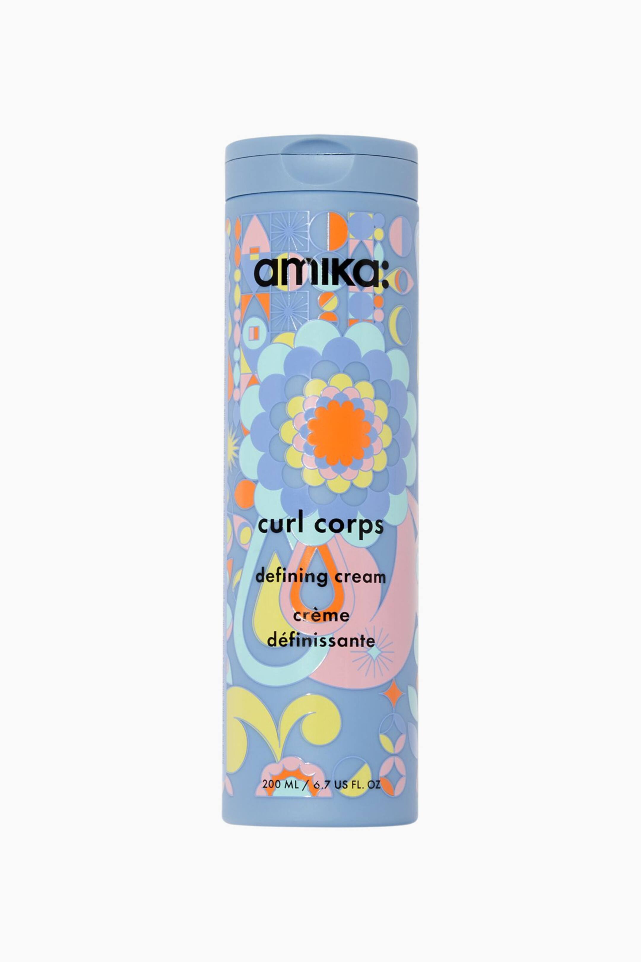 Näytä suurempi kuva: Curl Corps Defining Cream seisoo pystyasennossa vaaleansinisessä sylinterinmuotoisessa pullossa, jossa on siihen sopiva läppäkorkki, suoraan eteenpäin suunnattuna. Pullossa on värikäs, retrotyylinen kuviointi, jossa on kerroksittain kukka- ja geometrisia aiheita oranssin, keltaisen, pinkin ja sinisen sävyissä. Pullon etupuolella oleva musta teksti näyttää tuotemerkin "amika:" sekä tuotteen nimen "curl corps defining cream cr�me d�finissante."