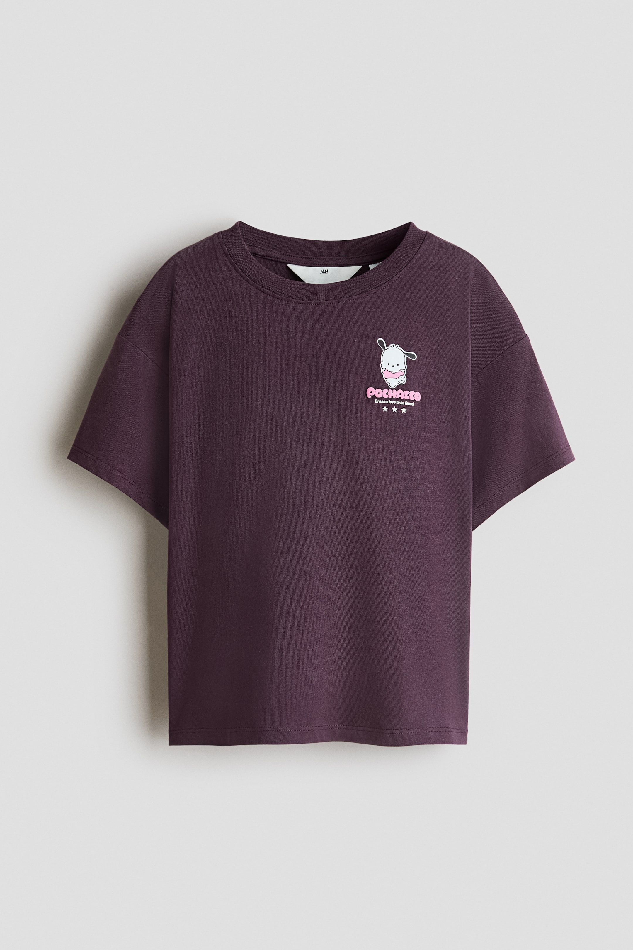 View larger image: A dark purple cotton jersey T-shirt is front-facing, featuring a round ribbed neckline, dropped shoulders, and short sleeves. A small graphic print of a cartoon dog character with pink text reading "POCHACCO" is detailed on the left chest.