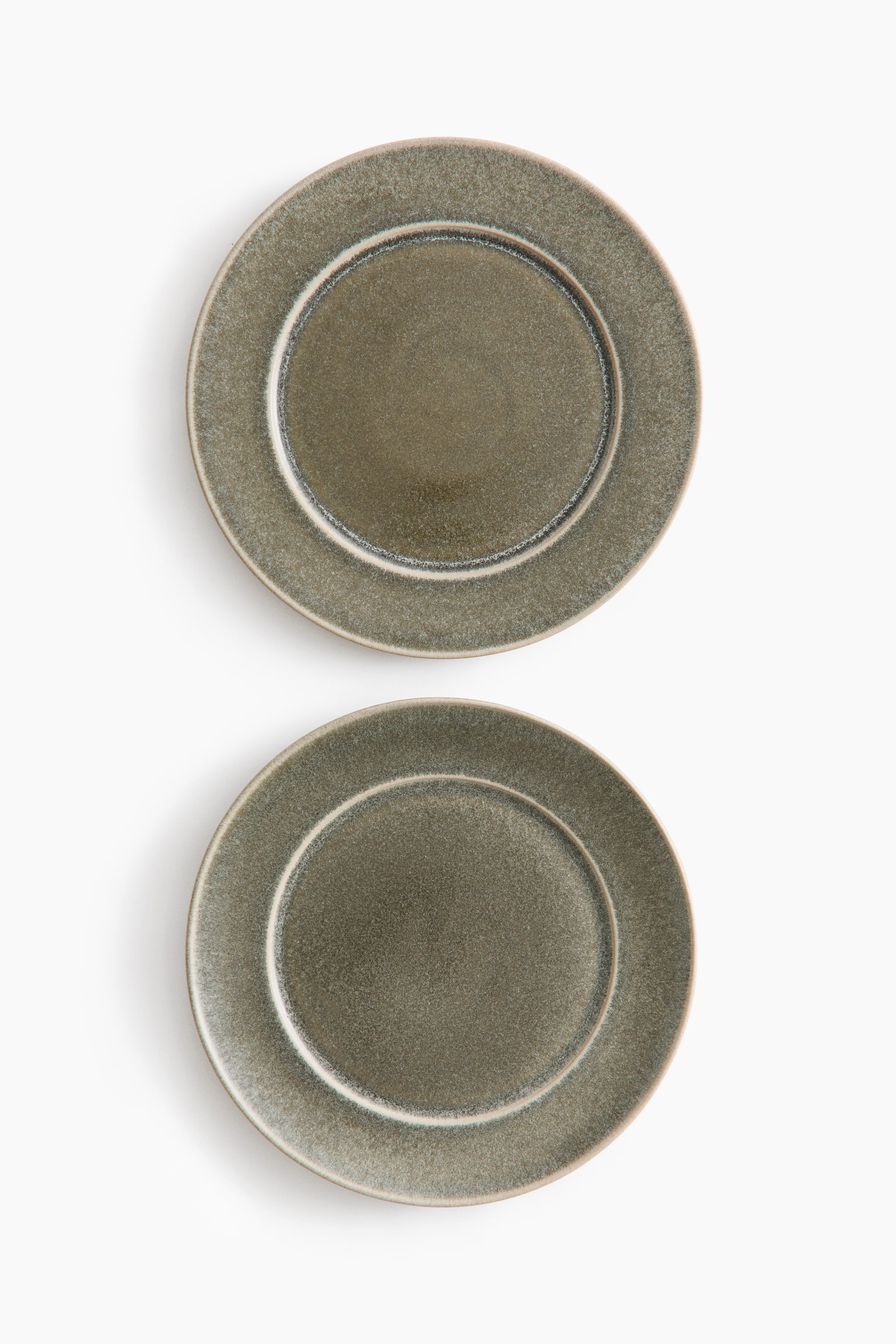 Dois pratos de cerÃ¢mica redondos apresentam um acabamento vidrado verde-oliva salpicado, com uma superfÃ­cie texturada e uma borda de cor clara. Os pratos estÃ£o virados para a frente numa vista de cima, dispostos verticalmente para destacar as suas formas circulares e as cavidades interiores bem definidas.