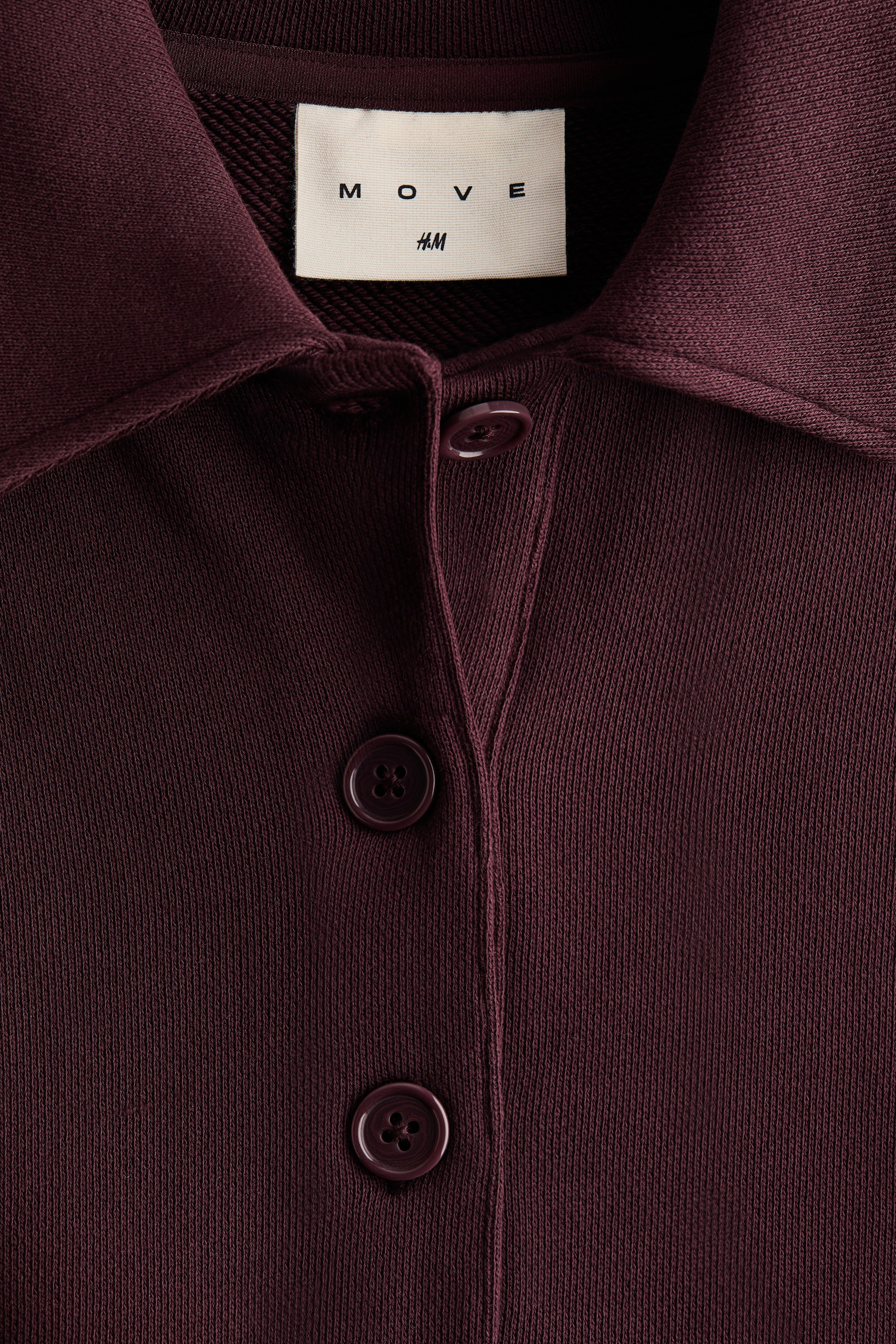 Grotere afbeelding bekijken: Een diep bordeauxrode gebreide top toont zijn voorkant, met een brede, platte kraag en een centrale knooplijst. Drie ronde, bijpassende knopen sluiten de knooplijst.