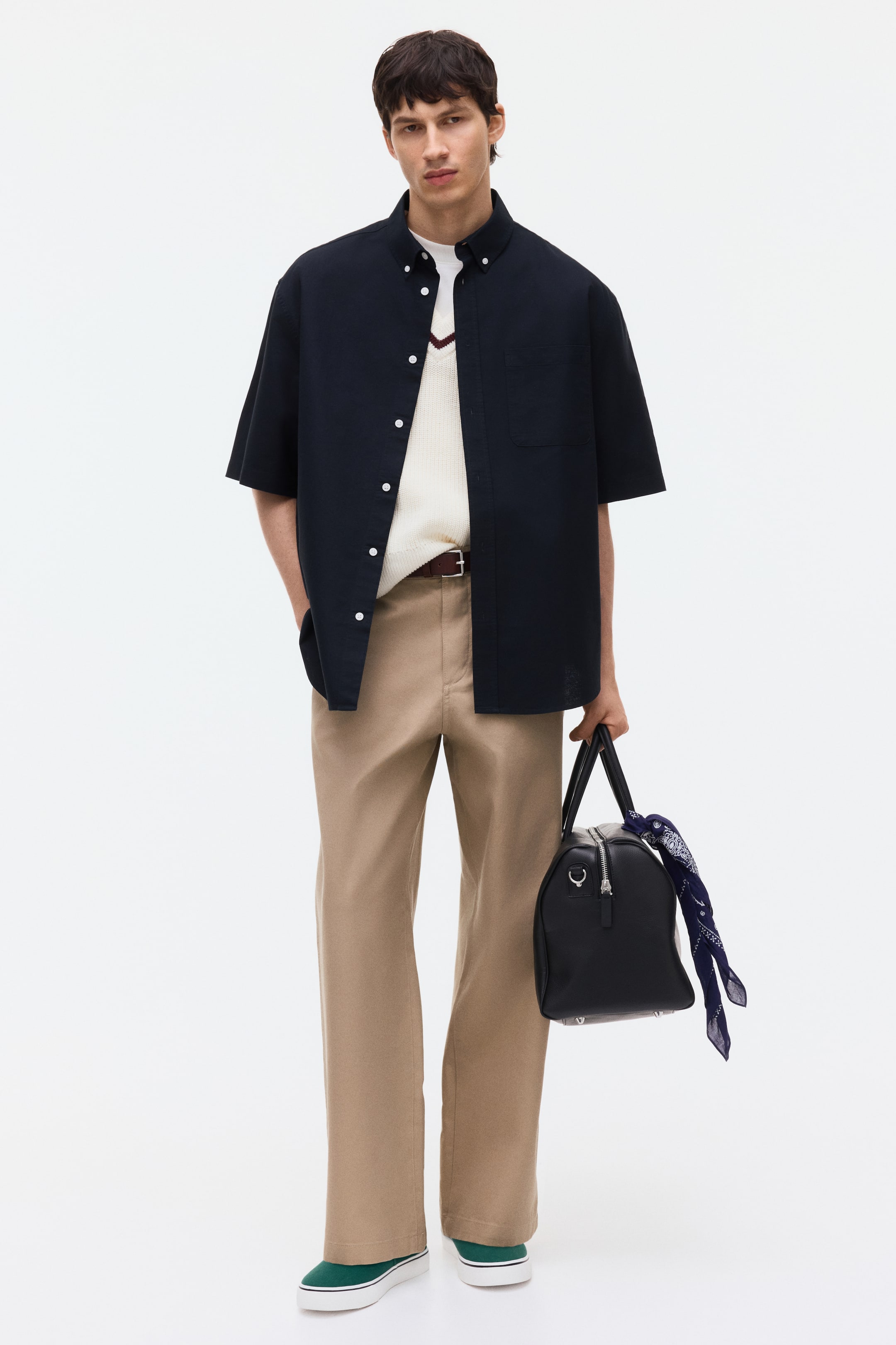 Xem ảnh lớn hơn: Một chiếc túi duffel màu đen đang được cầm bằng tay cầm trên, hướng về phía trước. Một chiếc khóa kéo màu bạc chạy dọc theo phần trên của túi, và các vòng chữ D có thể thấy ở hai bên. Một chiếc khăn bandana họa tiết xanh và trắng đang được buộc vào một tay cầm.