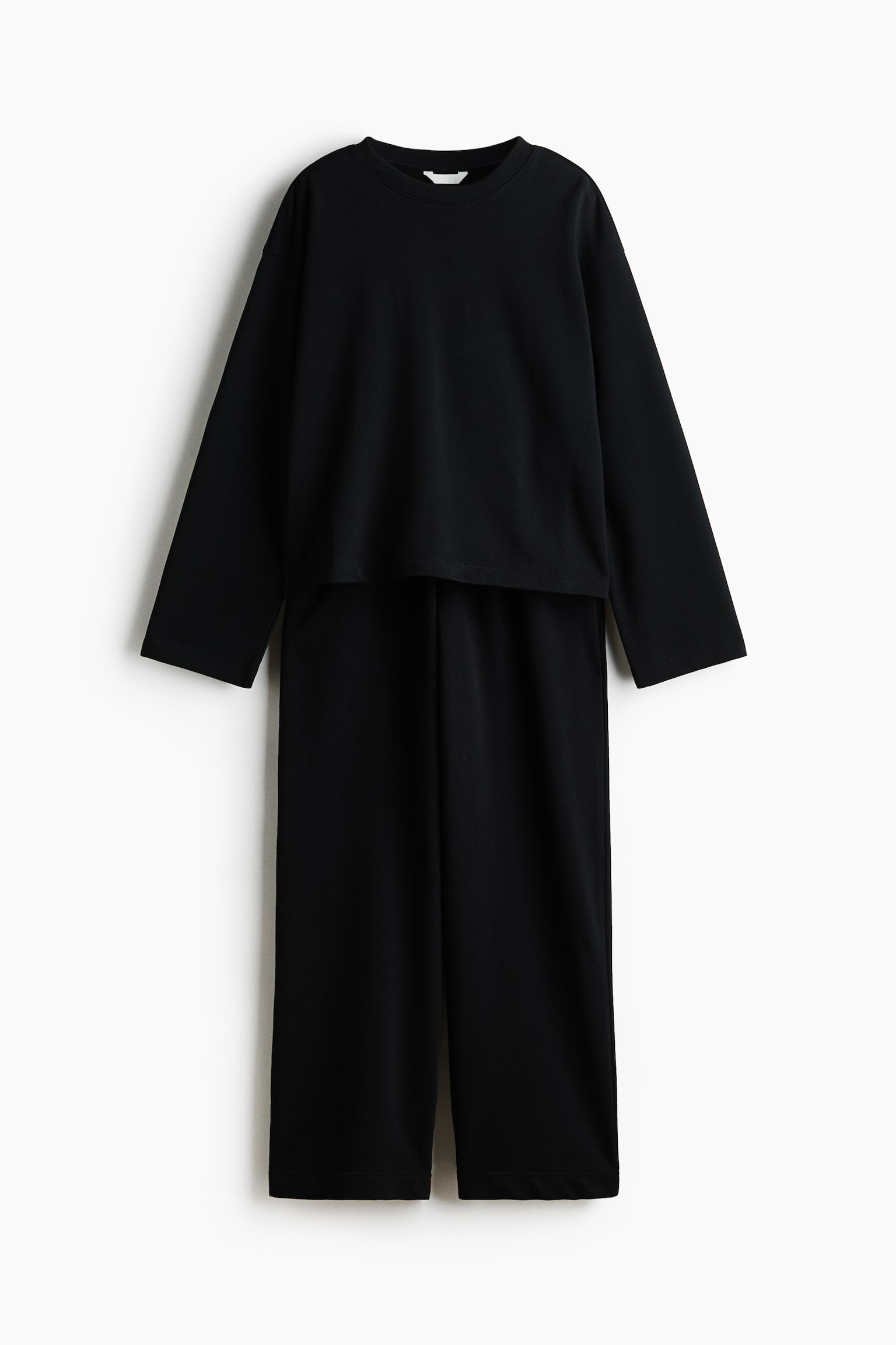 Een zwarte tweedelige loungewear set wordt frontaal gepresenteerd, met een losse, lange mouwen crew neck top en wijde pijpen broek. De cropped top rust over de lange broek, waarbij beide stukken een gladde, donkere stof tonen. - 1