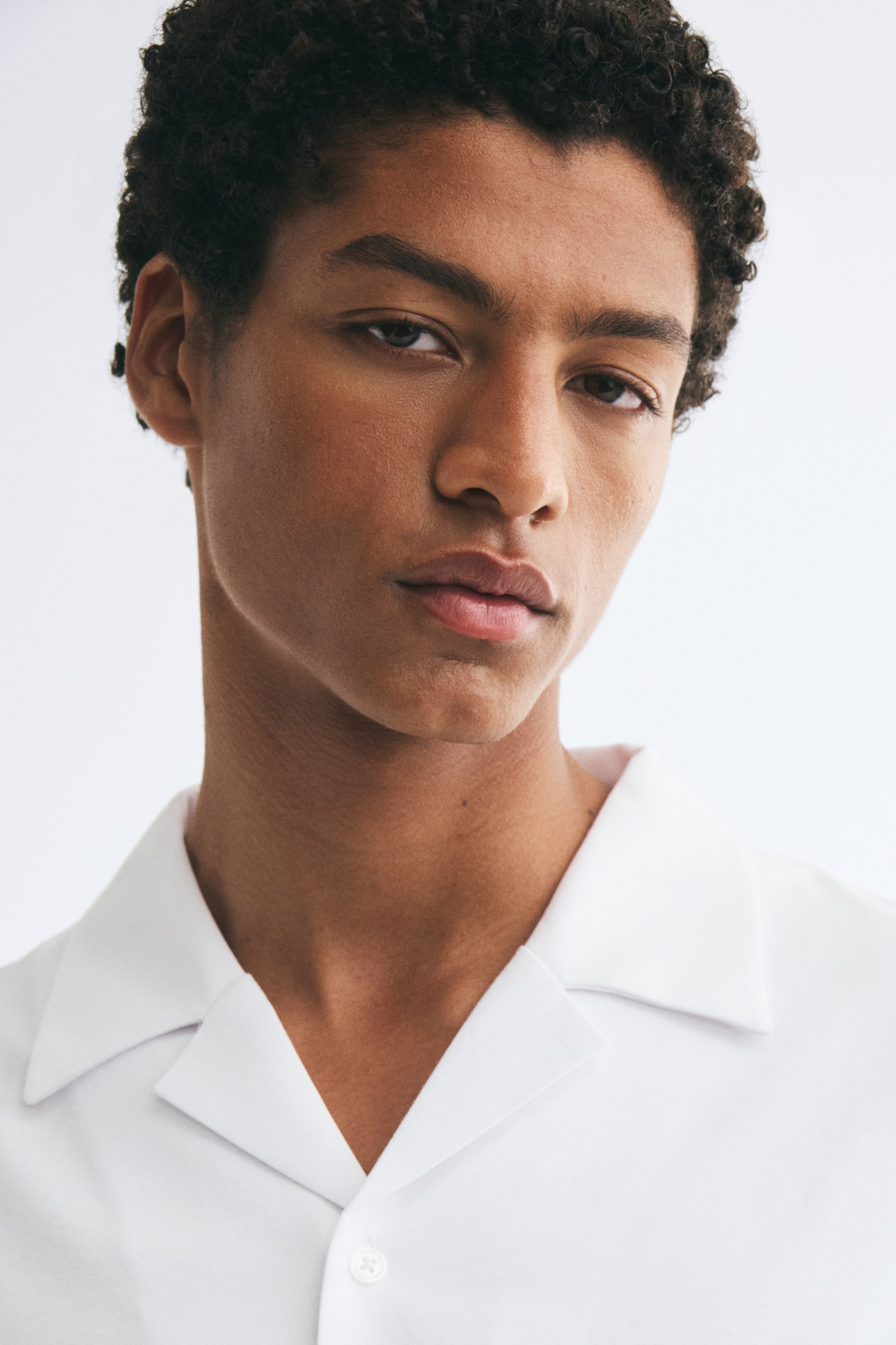 View larger image: A white cotton-blend jersey shirt featuring a resort collar is being worn by the model. This close-up view highlights the open collar design and a single white button on the front placket.