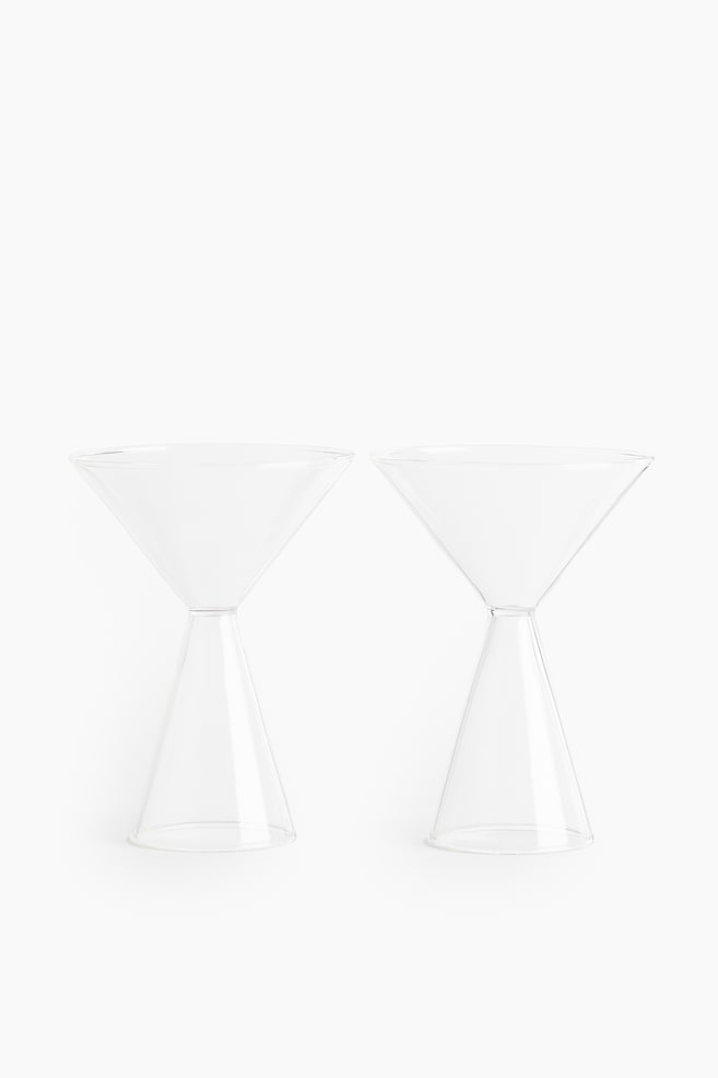 Two clear glass martini glasses are standing side-by-side, facing forward. Each glass features an inverted conical bowl that narrows to a short stem, which then widens into a conical base. - 1