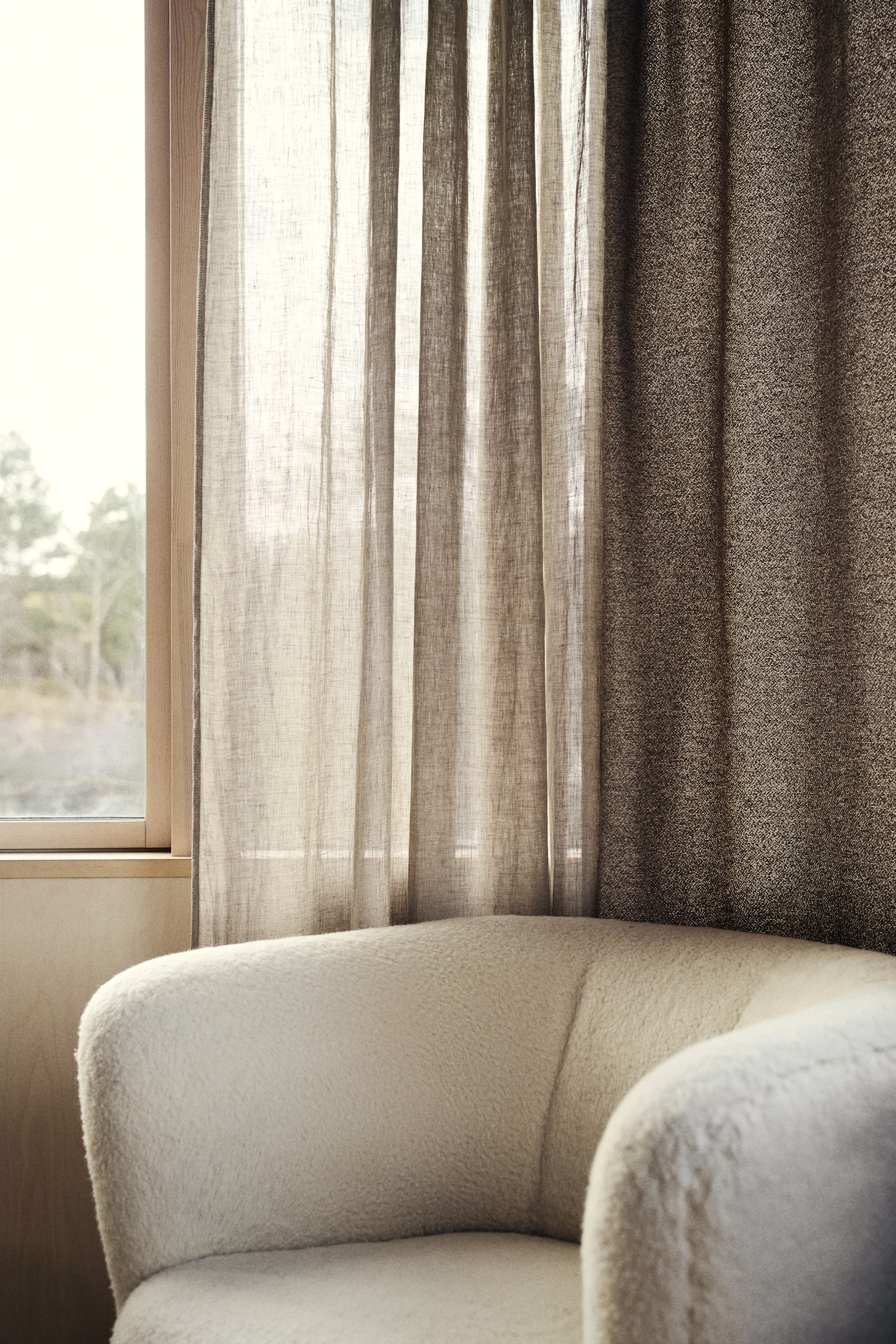 An off-white armchair is showcasing its rounded backrest and armrest, enveloped in a textured bouclé fabric. The chair's plush upholstery is visible from a slightly elevated side angle, accentuating its soft, curved design. - 1
