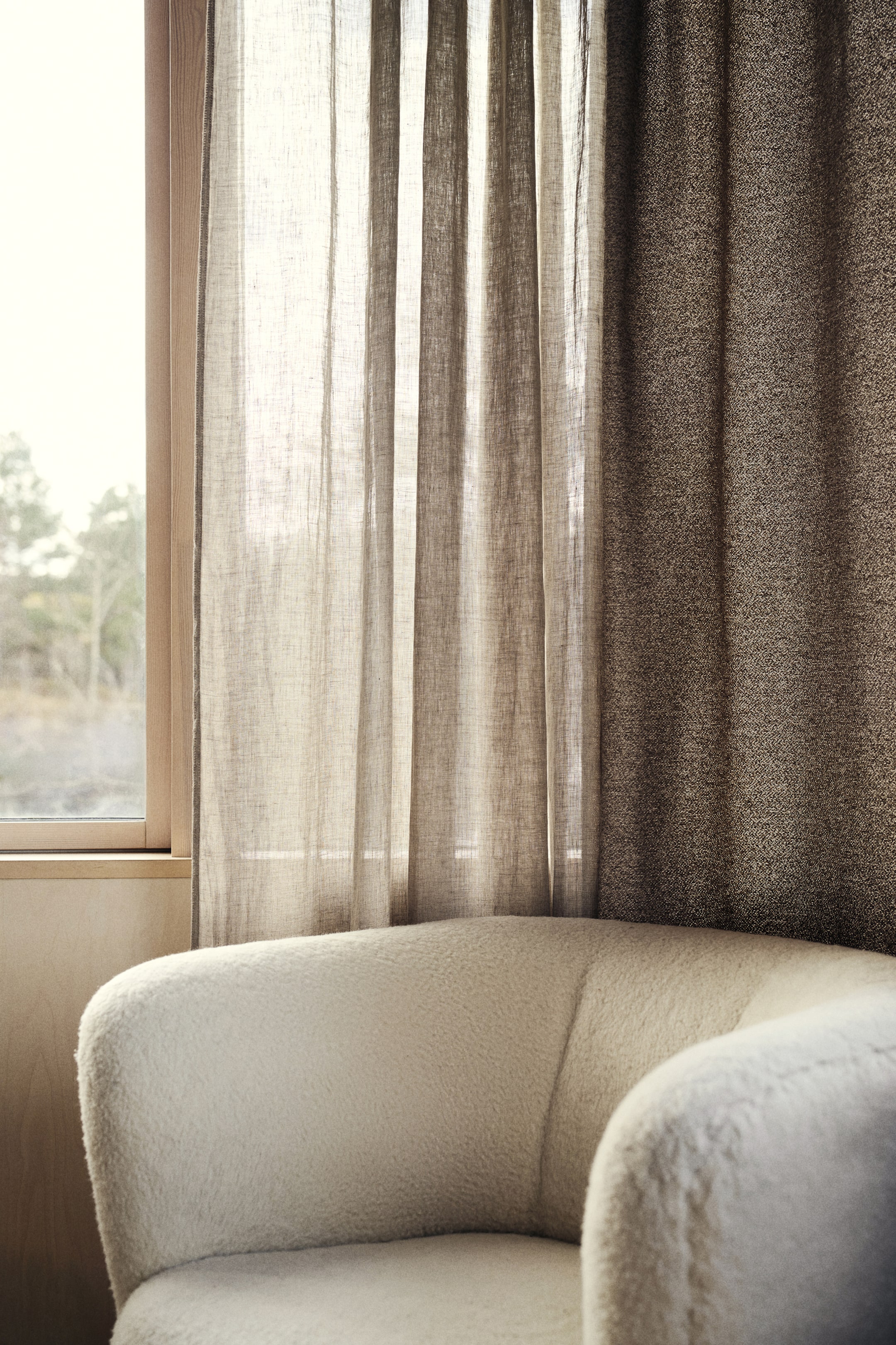 Grösseres Bild ansehen: Ein cremefarbener Sessel präsentiert seine abgerundete Rückenlehne und Armlehne, bezogen mit einem strukturierten Bouclé-Stoff. Die üppige Polsterung des Sessels wird aus einem leicht erhöhten Seitenwinkel gezeigt, wodurch das weiche, geschwungene Design hervorgehoben wird.