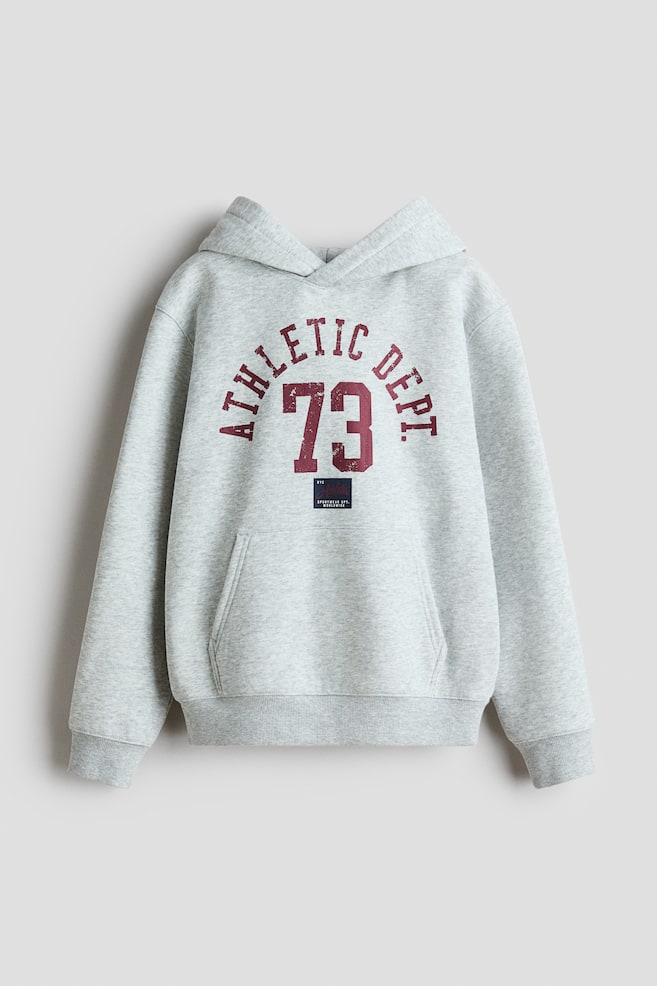 Ein hellgrauer Hoodie mit einem abgenutzten dunkelroten "ATHLETIC DEPT. 73"-Aufdruck auf der Vorderseite. Er ist mit einer Kapuze, einer Kängurutasche vorne sowie gerippten Bündchen und einem gerippten Saum designt. - 1