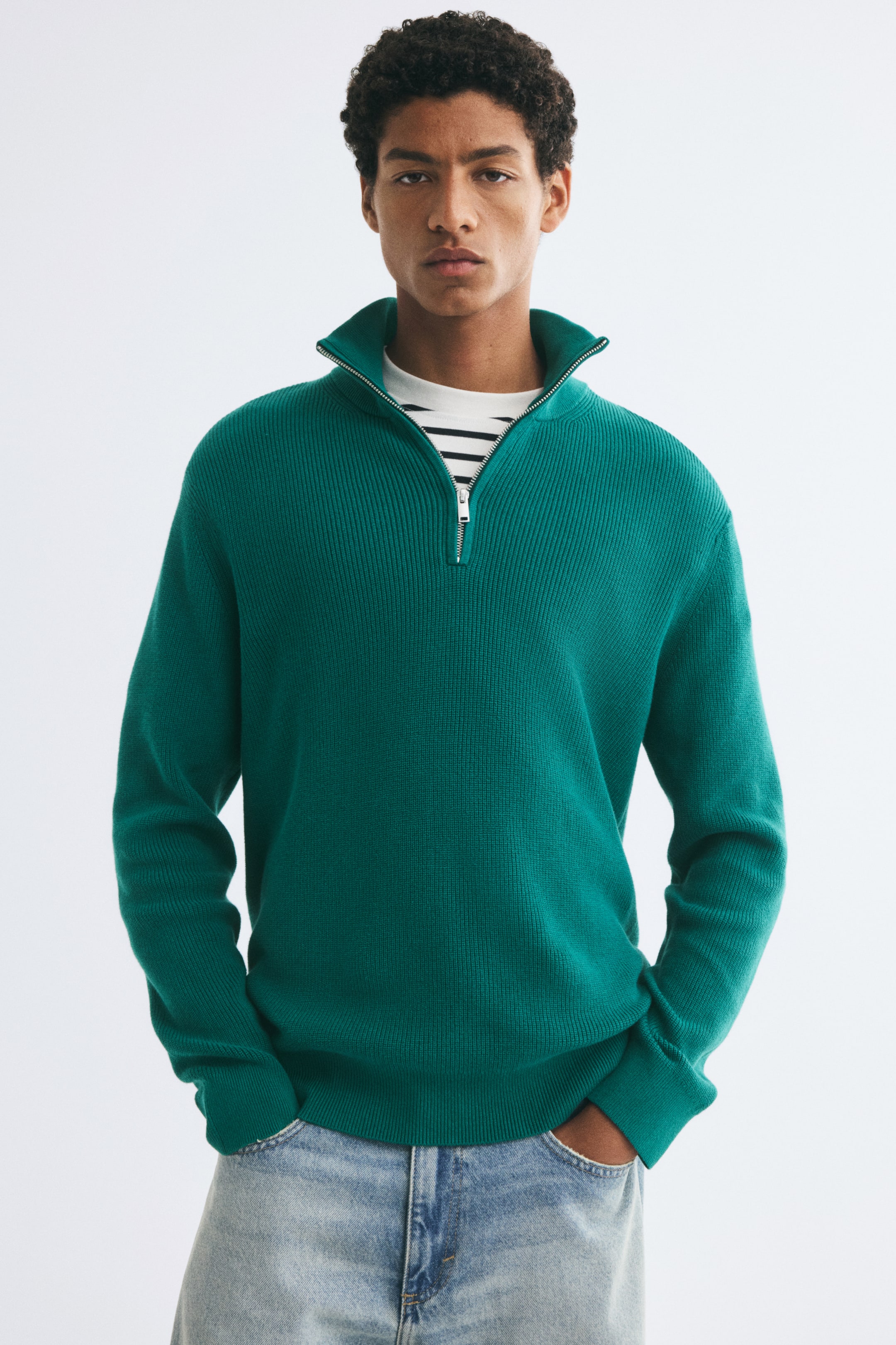 View larger image: A green rib-knit sweater featuring a stand collar with a silver half-zip is being worn by the model over a striped T-shirt. The sweater has a regular fit with ribbed cuffs and hem and is paired with light-wash jeans.