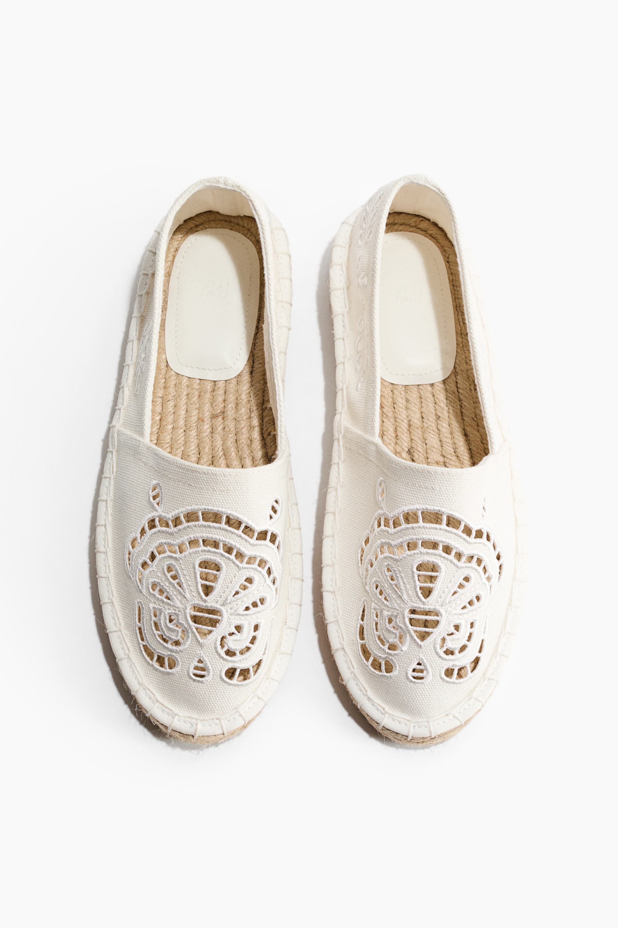View larger image: A pair of cream espadrilles is facing FRONT, displaying off-white canvas uppers featuring an ornate cut-out embroidery pattern on the toe box. The shoes are also showcasing braided jute soles and light cream insoles.