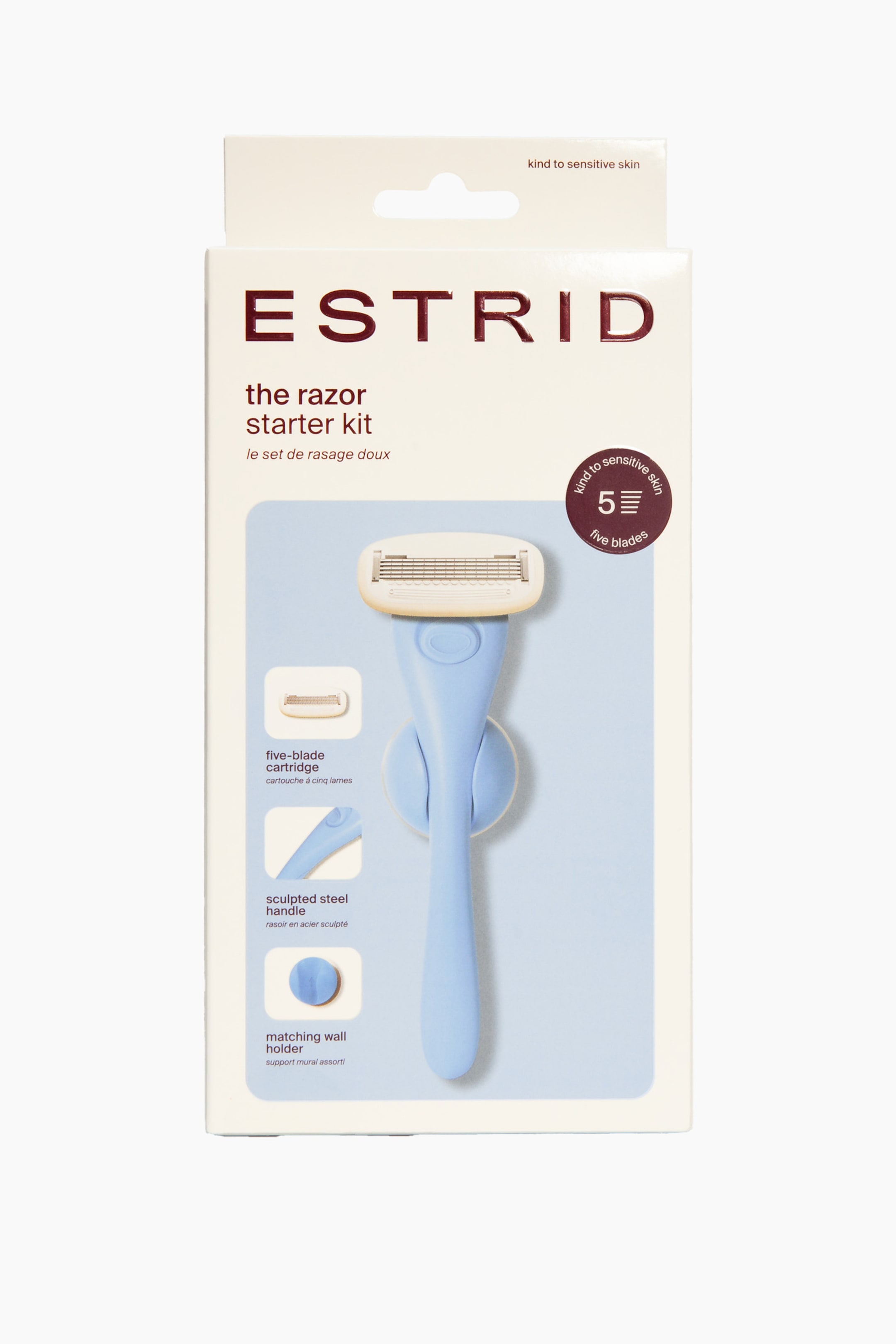 Näytä suurempi kuva: Estrid-partakoneen aloituspakkaus sisältää vaaleansinisen partakoneen, jossa on kermanvärinen viiden terän kasetti, esiteltynä luonnonvalkoisessa ja vaaleansinisessä pakkauksessaan. Pakkaus esittelee myös ylimääräisen viiden terän kasetin, veistoksellisen kahvan yksityiskohdan ja yhteensopivan pyöreän seinätelineen, ja siinä on teksti, joka osoittaa sen olevan hellävarainen herkälle iholle.