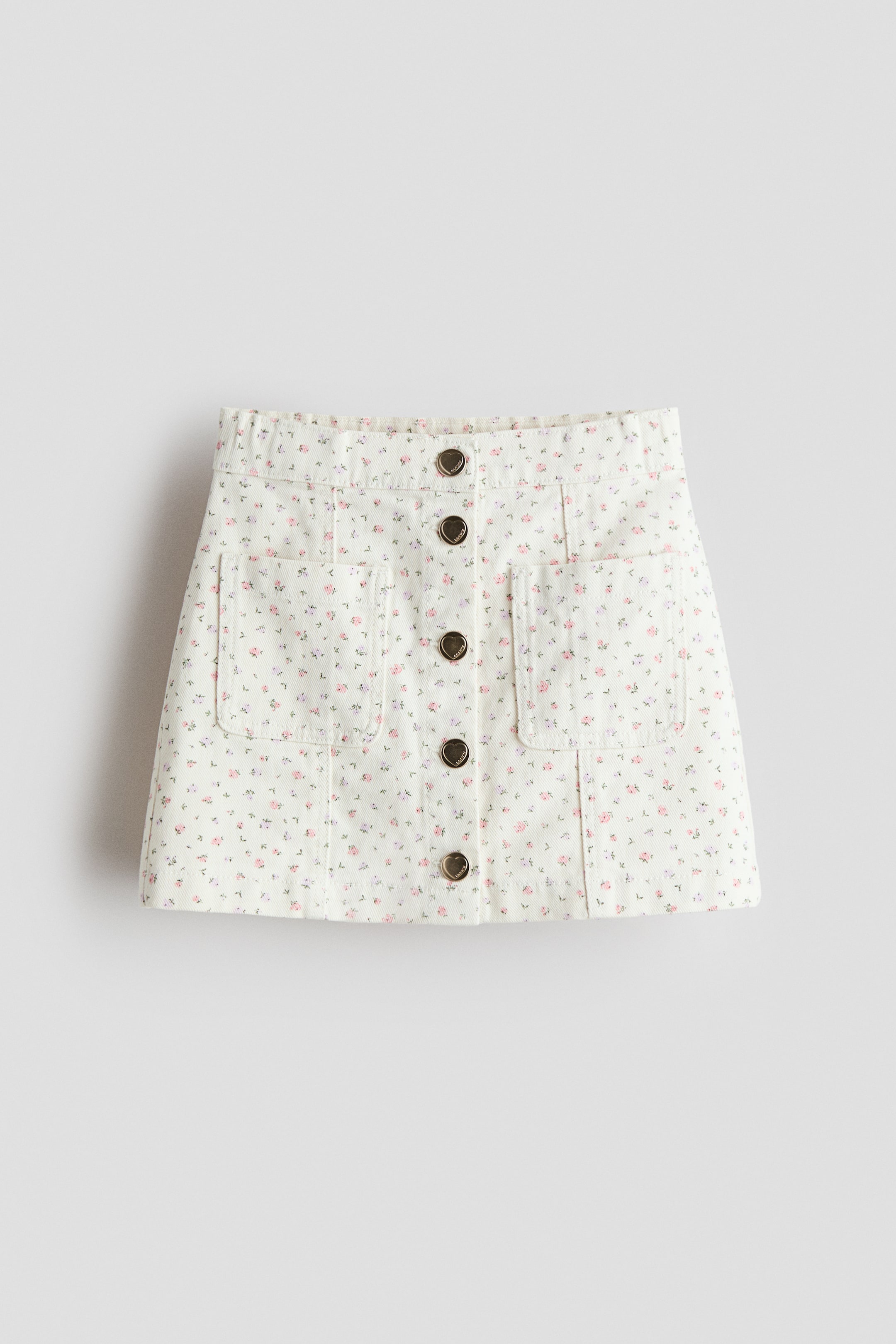 View larger image: Front view of a white cotton-twill skirt patterned with small pink, purple and green floral motifs. It features a row of press-studs down the centre front and two patch front pockets.