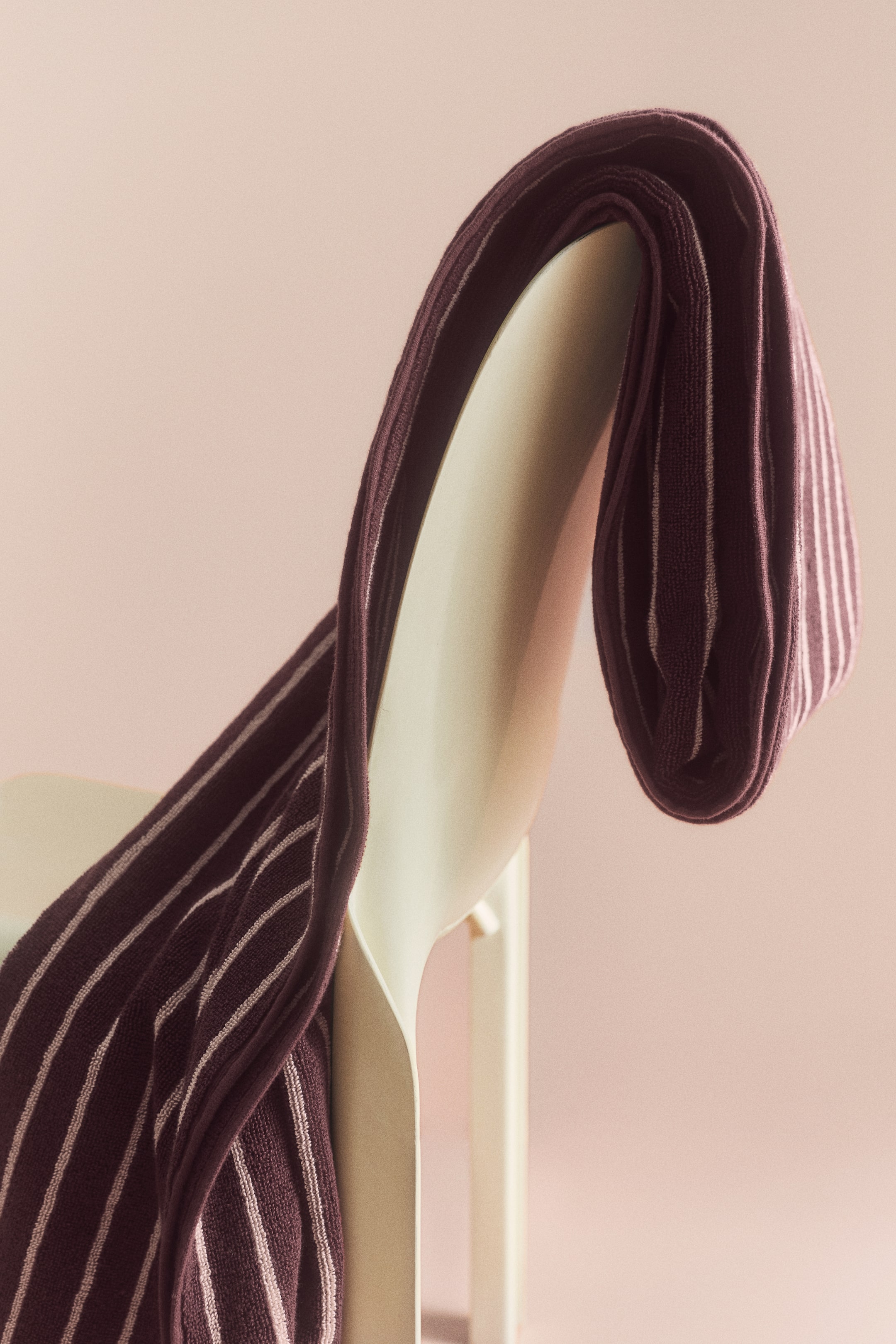 Visualizza l'immagine ingrandita: Un telo da bagno in spugna di cotone con un motivo a righe verticali bordeaux scuro e rosa chiaro è drappeggiato sullo schienale di una sedia color crema, mettendo in risalto il suo tessuto morbido e dalla texture ricca.