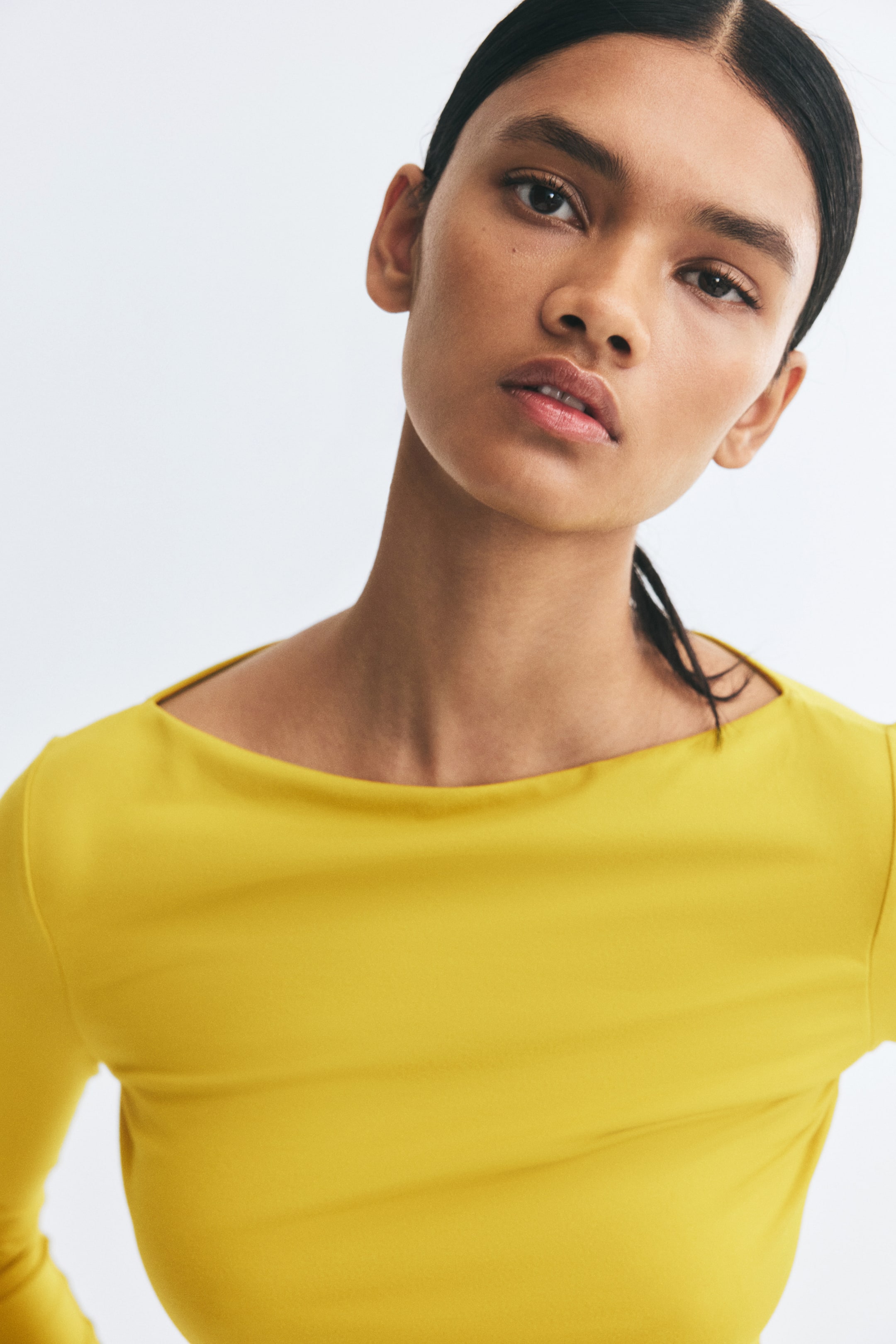 View larger image: The model is wearing a yellow fitted top with a wide boat neck and long sleeves.
