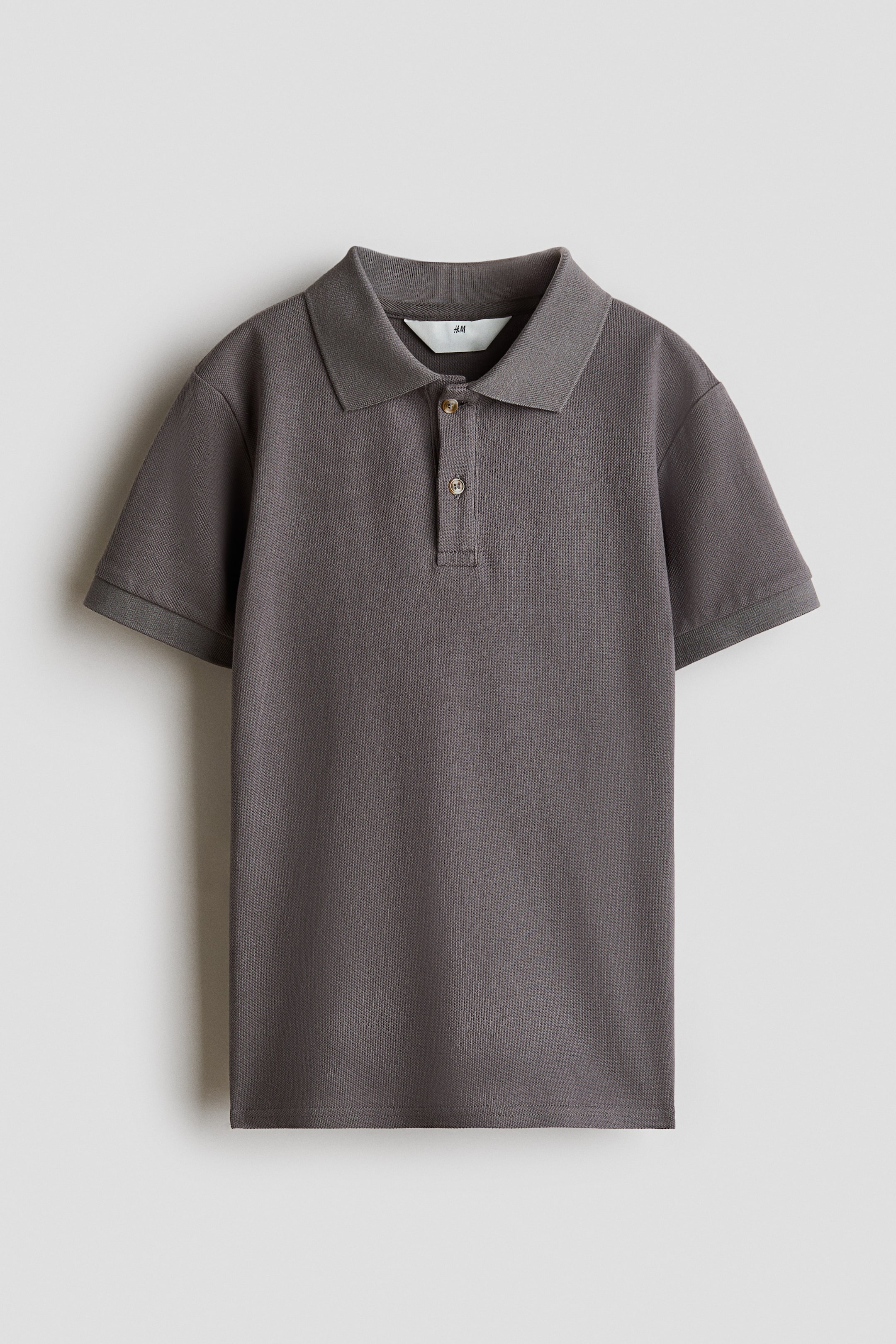 View larger image: A dark grey polo shirt is facing forward, featuring a classic collar, a two-button placket, and short sleeves with ribbed cuffs. The shirt is displaying a textured piqué knit fabric and a straight hem.