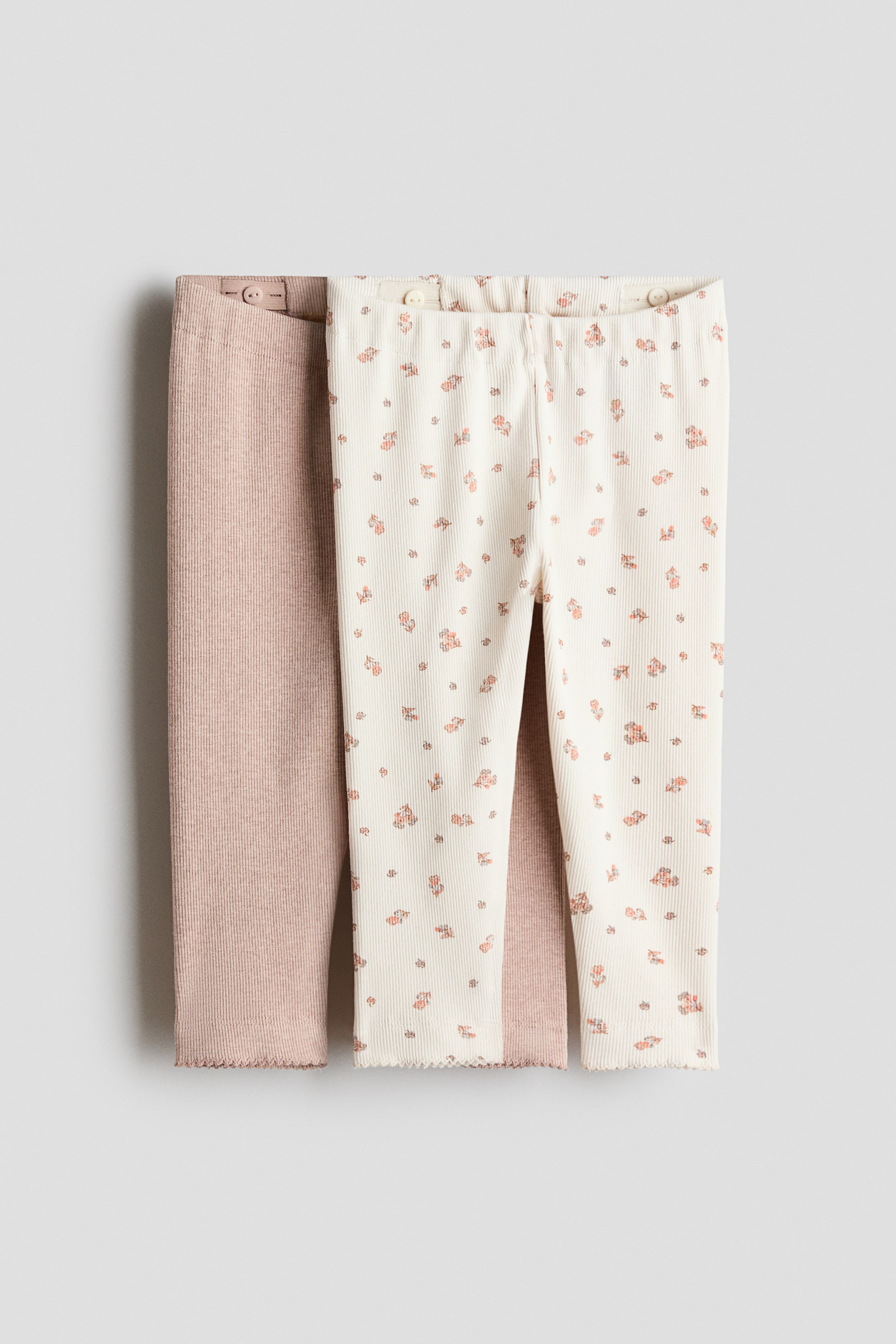 Ampliar la imagen: Se presentan dos pares de leggings de jersey acanalado desde el frente. Un par en color marrón claro está parcialmente superpuesto a un par en color blanco roto, que presenta un pequeño patrón floral. Ambos leggings muestran una elasticidad ajustable en la cintura y dobladillos con borde de picot.