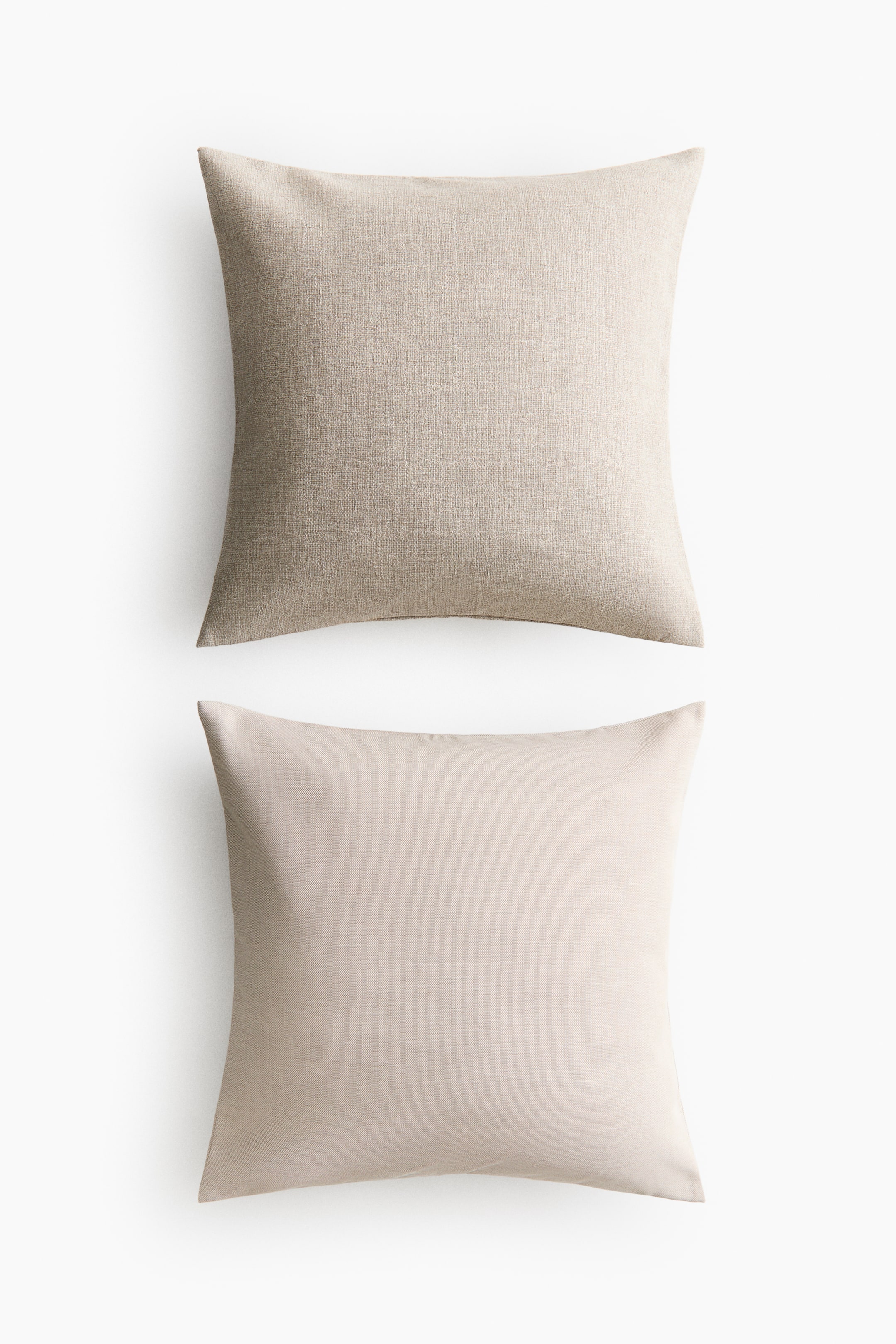 View larger image: Two square throw pillows are displayed from the front, stacked vertically. The top pillow features a light beige color with a prominent woven texture, while the bottom pillow showcases a lighter, fine-textured beige.