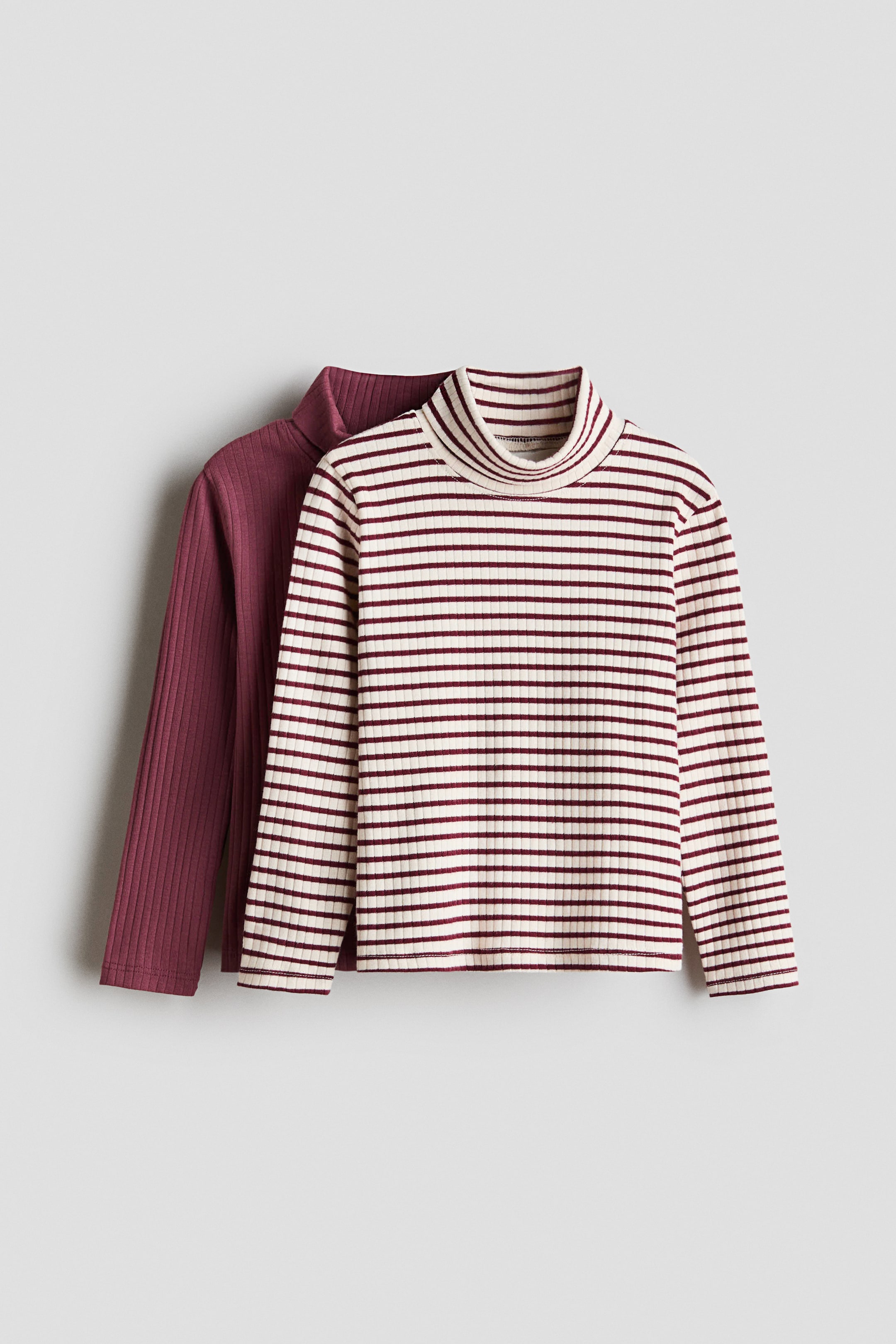 View larger image: H&M Adorables long-sleeved tops are on display. The front top is a cream ribbed jersey featuring horizontal dark red stripes and a foldover polo neck, while a solid dark red ribbed jersey top is positioned slightly behind and to the left.