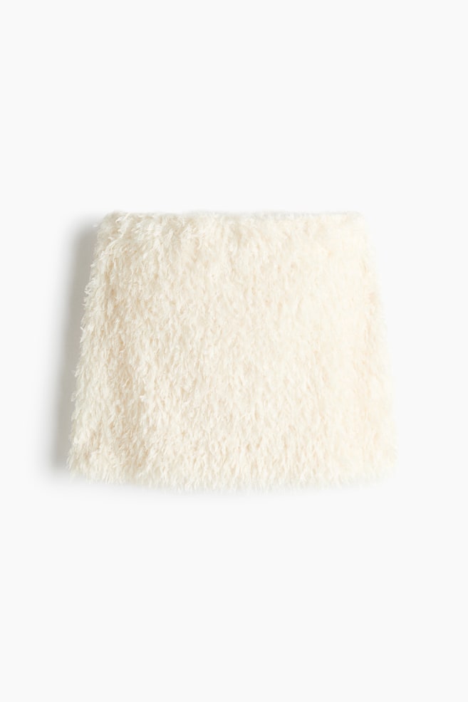 A cream-coloured mini skirt is shown from the front, featuring a highly textured, shaggy, fluffy fabric with a slightly flared A-line silhouette. - 1