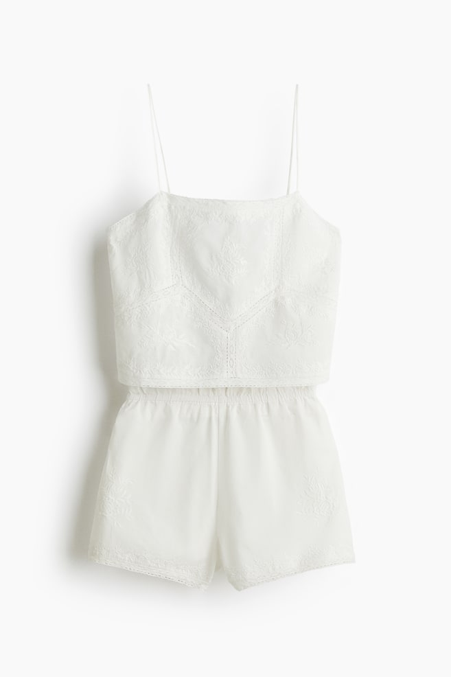Ein weißes Pyjama-Set wird von vorne präsentiert, bestehend aus einem Trägertop und passenden Shorts in Baumwollgewebe. Das Top ist mit Ton-in-Ton-Stickerei und Spitzenbesatz versehen, während die Shorts einen elastischen Bund, passende Stickereien und Spitze entlang des Saums aufweisen. - 1