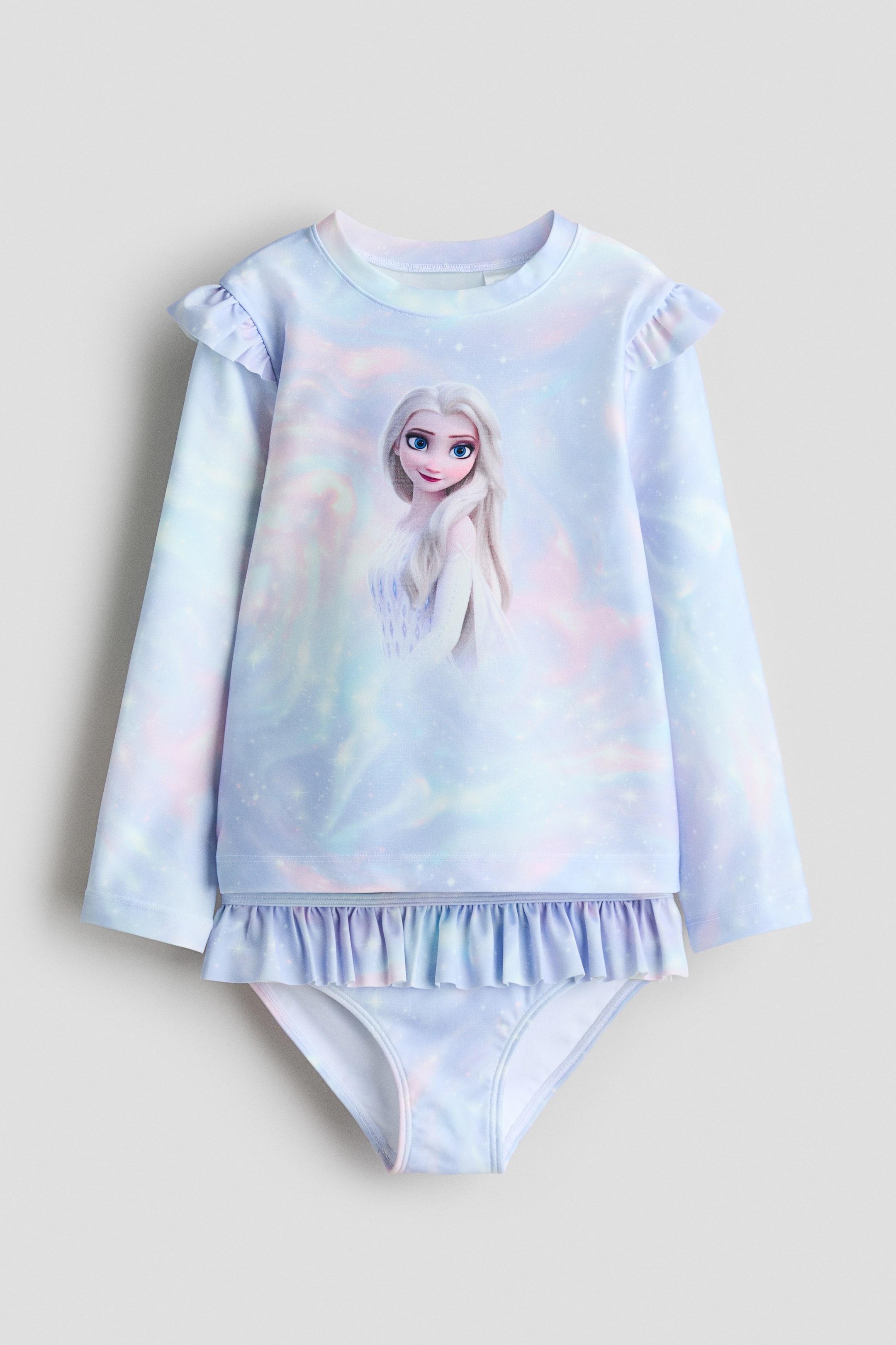 View larger image: Shown from the front: a children's two-piece swimsuit. The long-sleeved top features a graphic of Elsa from Frozen on a light-blue, pink and purple iridescent background with small star-like speckling, while ruffles trim the shoulders and hem. Matching briefs complement the top.