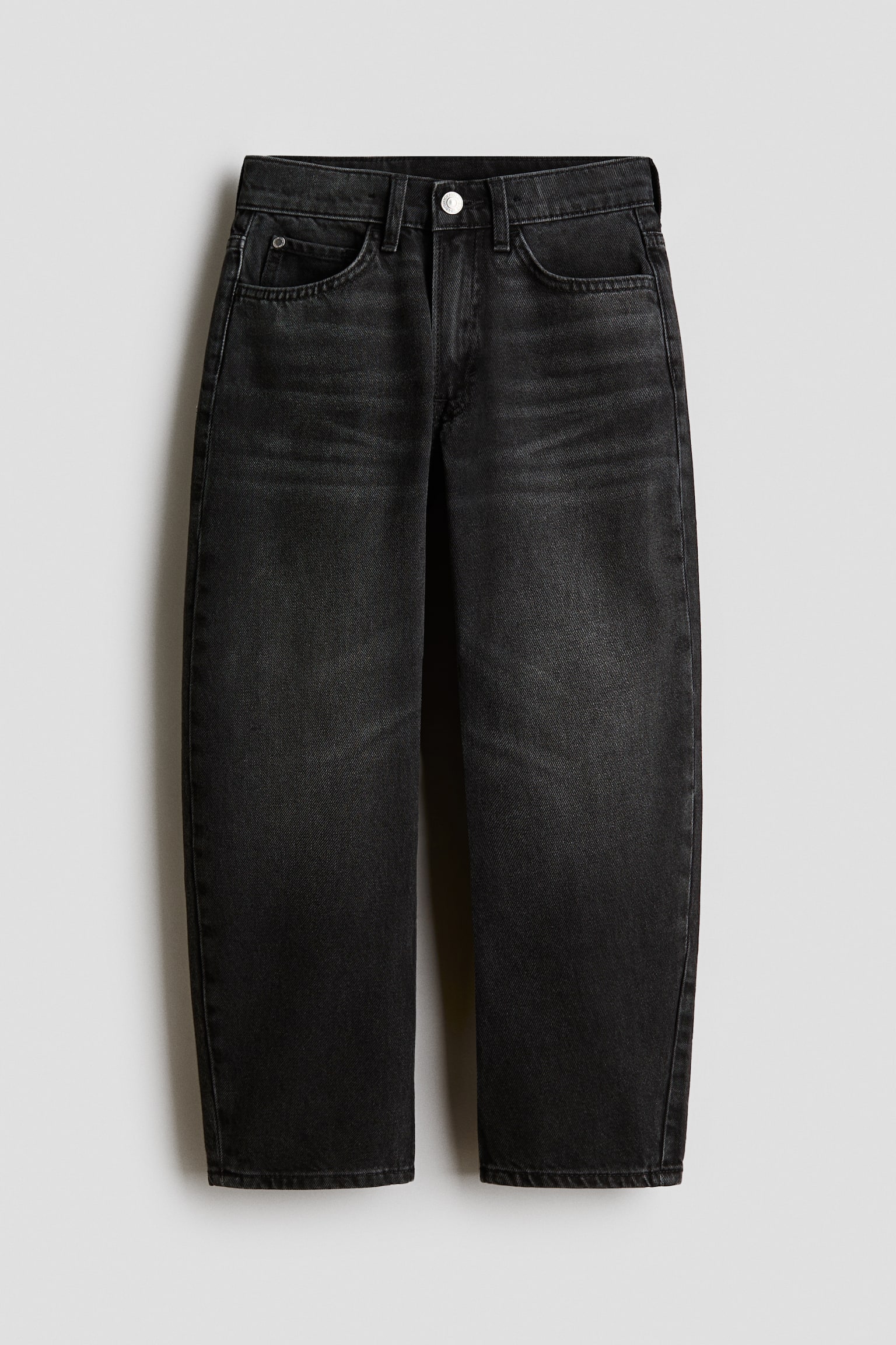 Ett par blekta svarta jeans i denim visas framifrÃ¥n, med en avslappnad, rak benvidd. Jeansen har en klassisk femficksdesign, bÃ¤lteshÃ¤llor, en enkel silverfÃ¤rgad knappknÃ¤ppning och diskreta slitningar Ã¶ver de Ã¶vre lÃ¥ren.