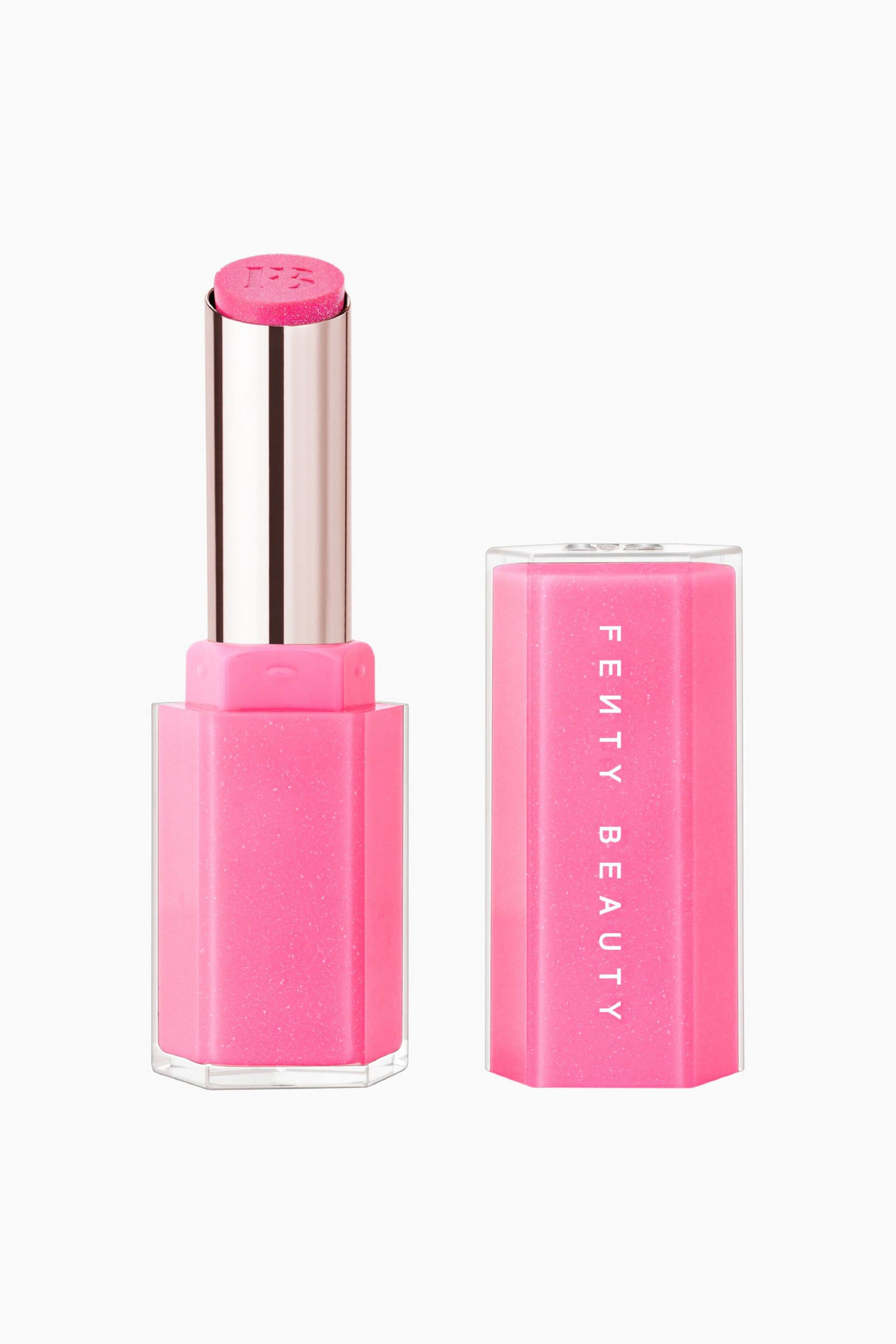 Näytä suurempi kuva: Gloss Bomb Stix High-shine Shimmer Gloss Stick seisoo pystyasennossa irrotetun korkkinsa vieressä, esitellen kirkkaan vaaleanpunaisen, hohtavan ja “FB”-kohokuvioidun stick-osan, joka työntyy esiin metallinhohtoisesta hopeisesta tuubista. Sekä kuusikulmainen pohja että siihen kuuluva korkki sisältävät kimaltavan vaaleanpunaisen sisäytimen, joka on koteloitu kirkkaaseen akryyliin, ja korkissa lukee pystysuunnassa valkoisella “FENTY BEAUTY”.